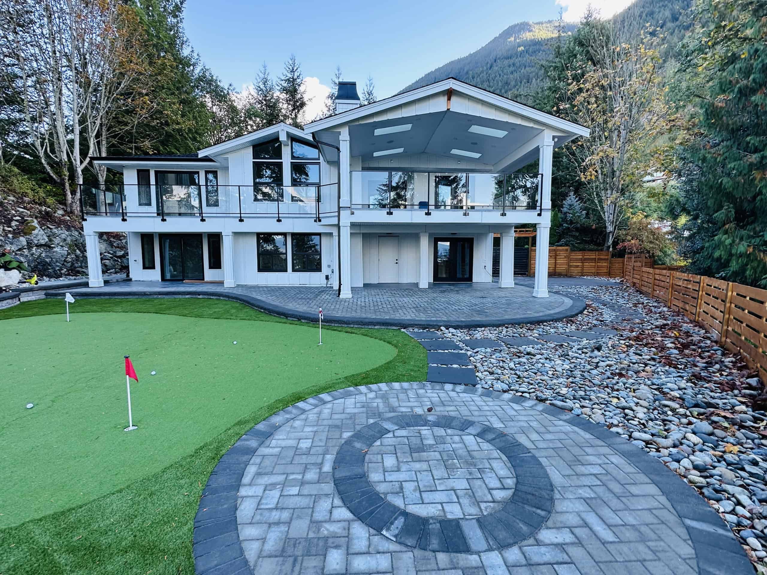 Modern waterfront home with spacious decks, lush landscaped yard, and a private putting green, perfect for outdoor living and entertainment in coastal British Columbia.