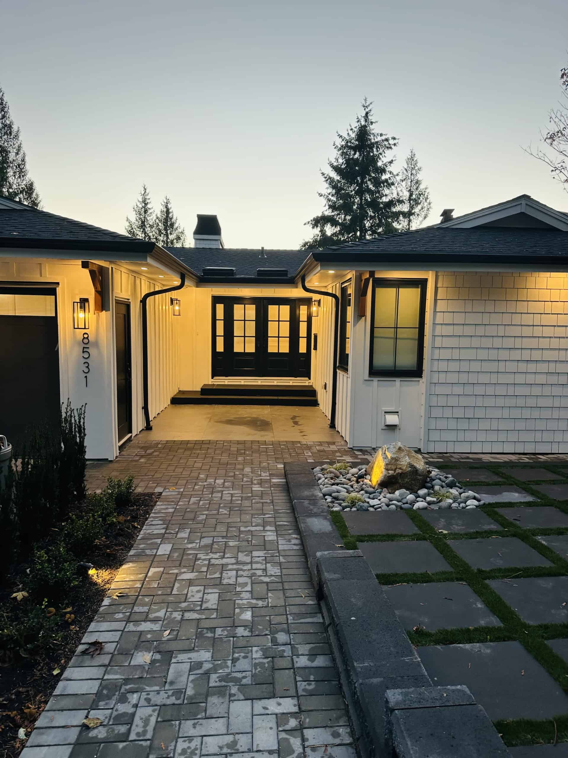 Charming modern house entrance with a paved walkway, front porch lighting, and landscaped garden, showcasing professional real estate services by Orca Realty Inc.