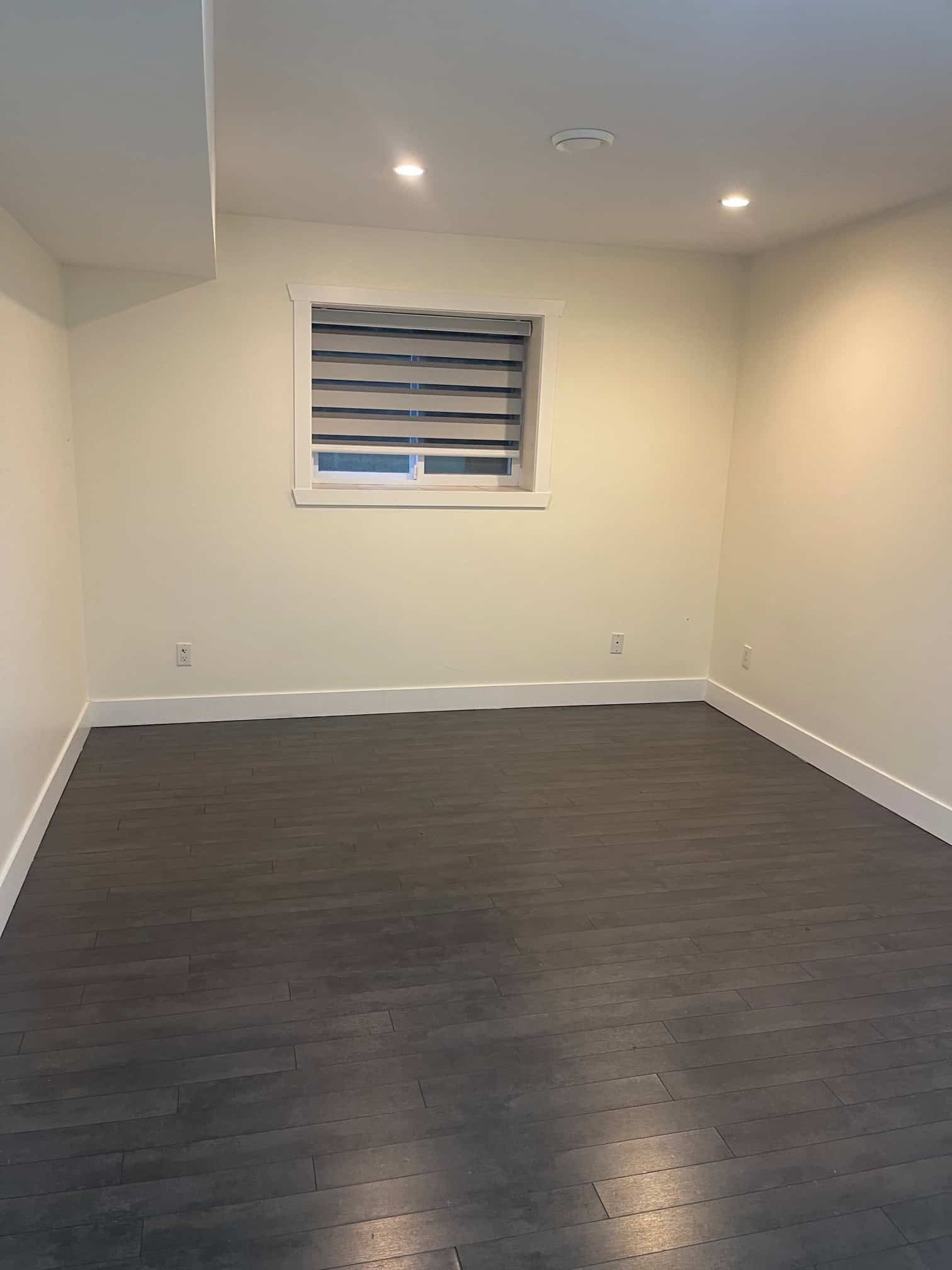 Bright modern interior room with white walls, dark wood flooring, and a window with horizontal blinds, showcasing professional residential property for sale or rent by Orca Realty Inc.