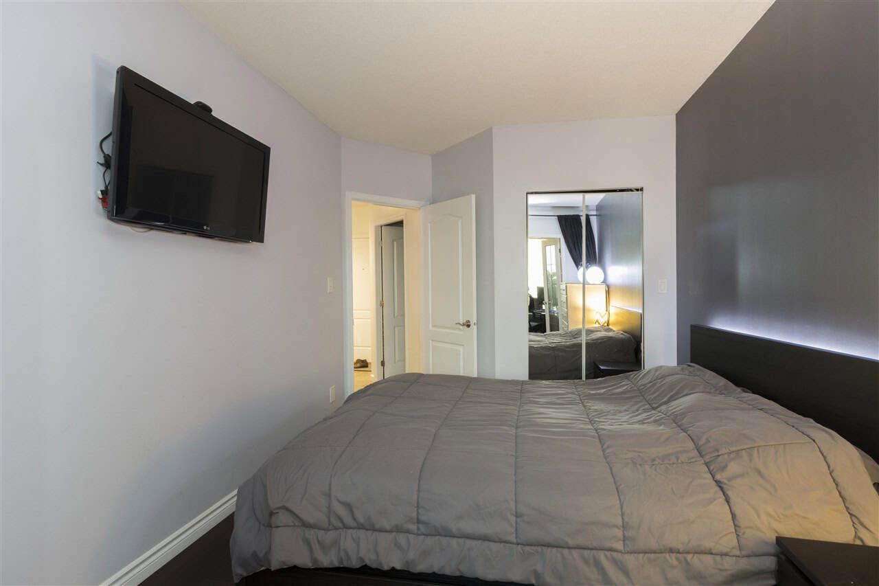 Modern bedroom with grey walls, mirrored closet doors, and a wall-mounted flat-screen TV — ideal for Vancouver area real estate listings.