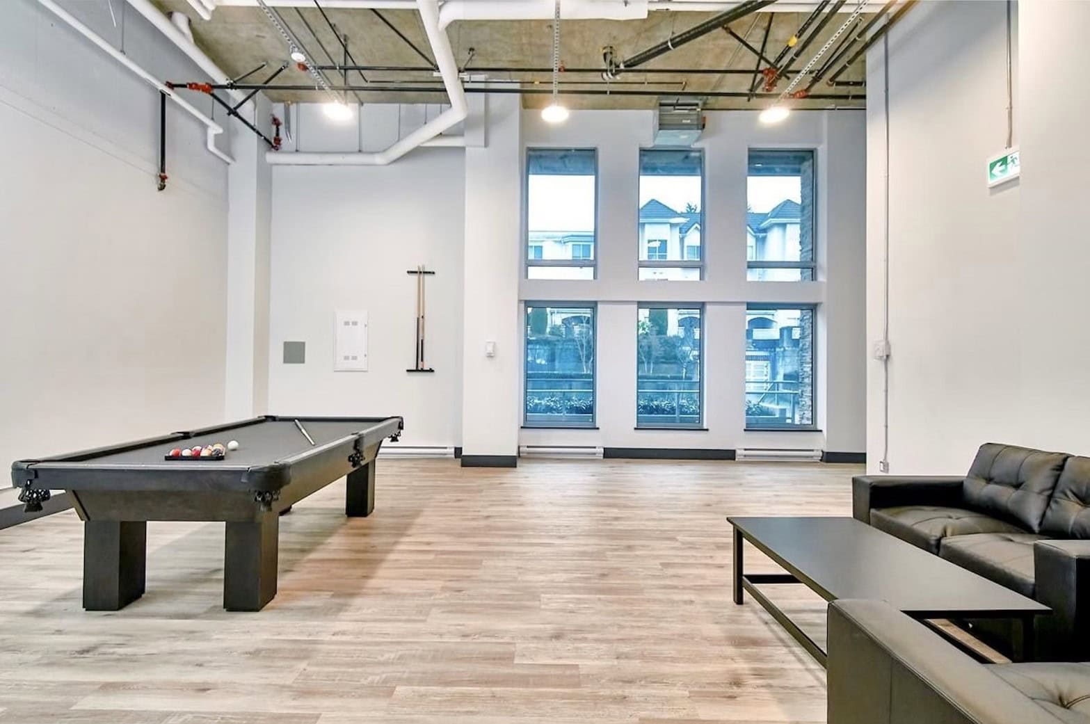 Modern indoor recreational area with pool table, comfortable black leather sofa, and large windows in a commercial or residential building. Ideal for relaxation and social gatherings.