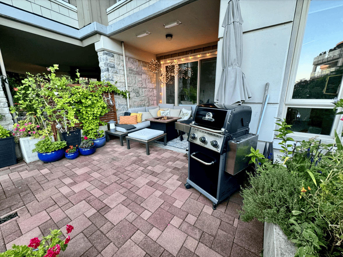 Outdoor patio with comfortable seating, lush plants, and a gas grill, perfect for relaxing or entertaining in a modern urban apartment in Vancouver. Well-maintained space with decorative lighting.