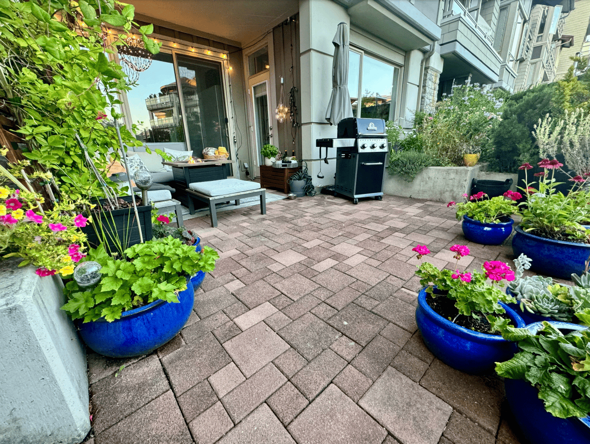 Vibrant outdoor patio with lush potted plants, cozy seating area, and a barbecue grill, perfect for enjoying outdoor living and entertaining in a modern urban setting.