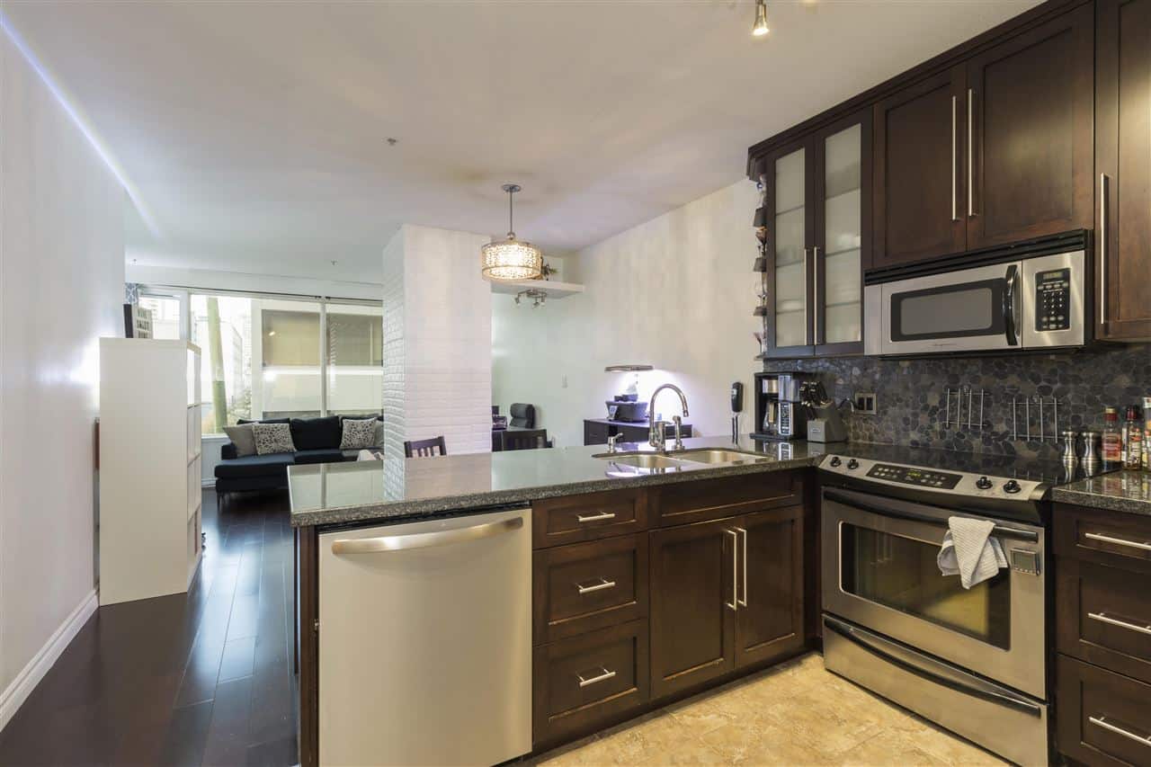 Modern kitchen with dark wood cabinets, stainless steel appliances, granite countertops, and open-concept living space in a Vancouver waterfront condo, perfect for luxury BC real estate buyers.