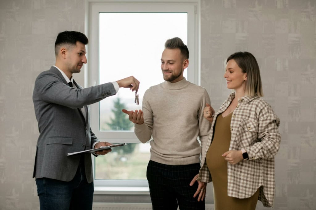 Real estate agent handing keys to happy couple in a new home, representing property buying or selling services offered by Orca Realty Inc. in Vancouver, BC.