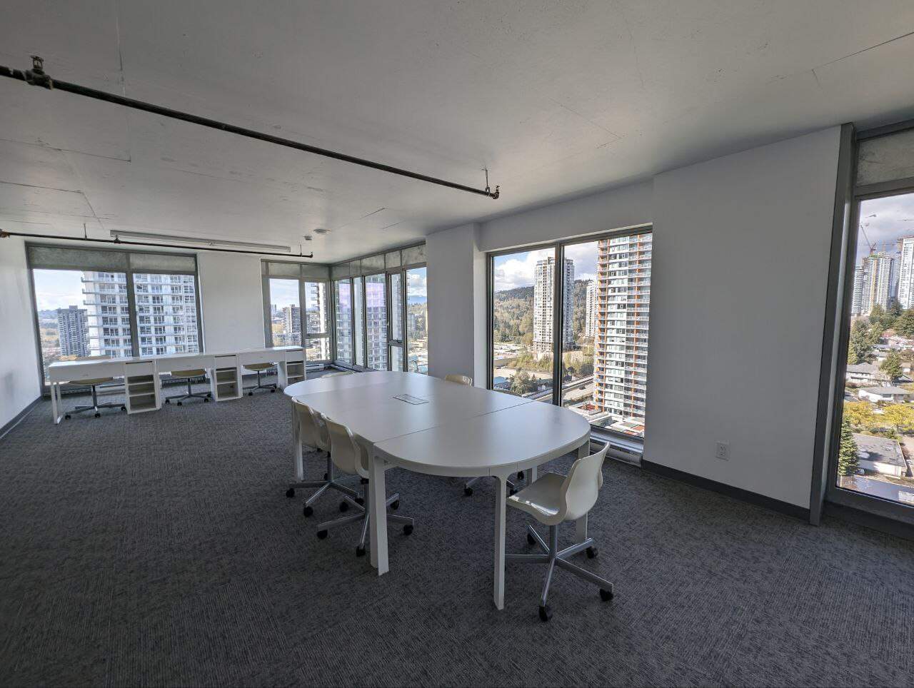 Bright modern office space with large windows offering panoramic city views, ideal for corporate or coworking environments, featuring a conference table and ergonomic chairs.