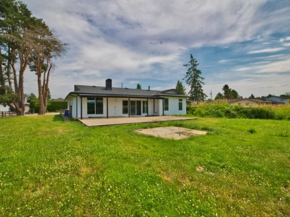 Spacious backyard of a modern residential home with a lush green lawn, mature trees, and a wooden deck, ideal for outdoor living and relaxation, in a peaceful neighbourhood.
