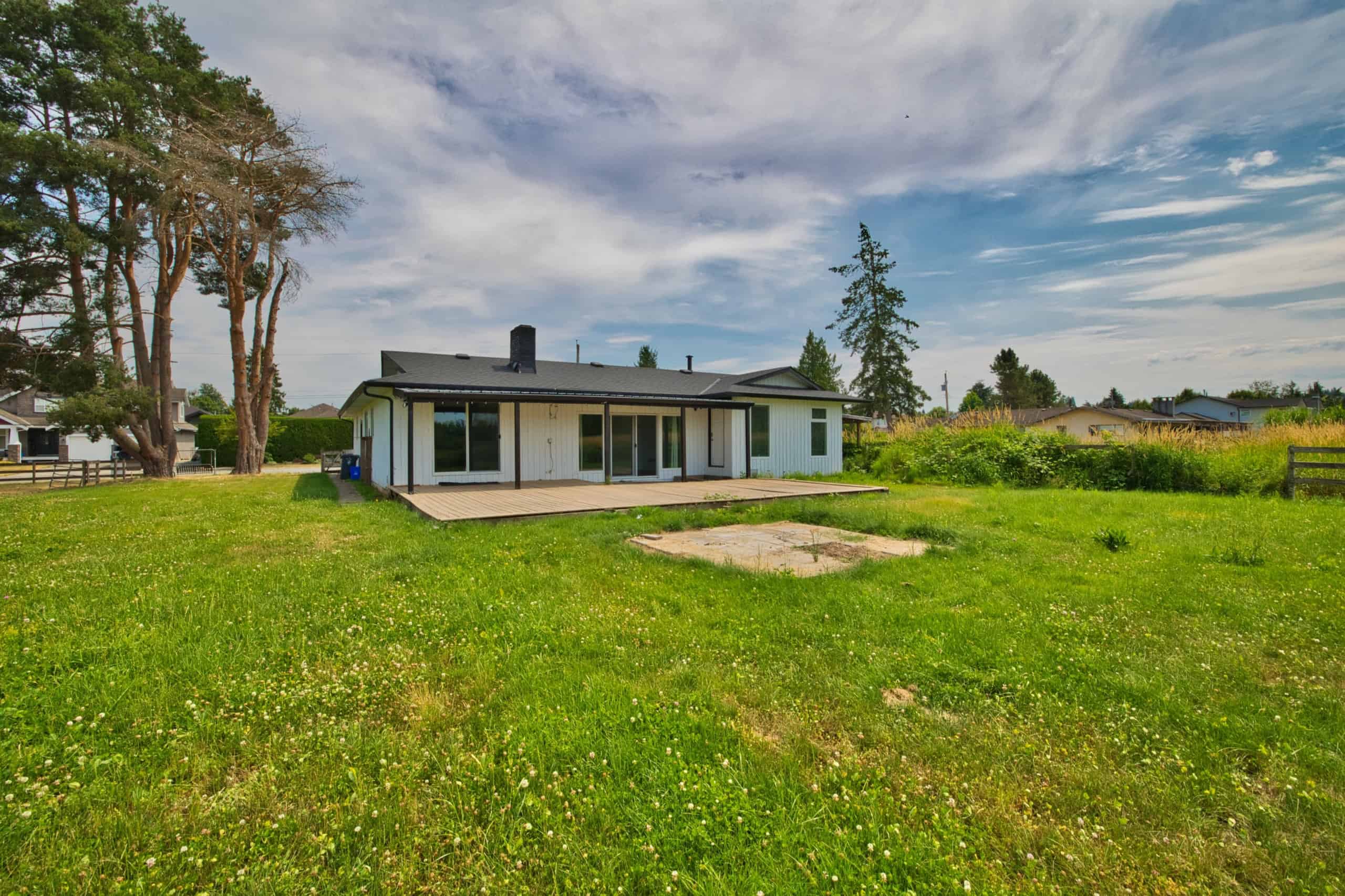 Spacious backyard of a modern residential home with a lush green lawn, mature trees, and a wooden deck, ideal for outdoor living and relaxation, in a peaceful neighbourhood.
