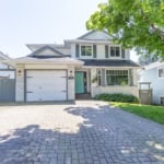 Bright two-story white and grey house with a front driveway, lush greenery, and a welcoming entrance, perfect for Vancouver real estate buyers seeking charming family homes in the area.