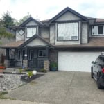 Spacious modern house with grey siding, stone accents, and a landscaped front yard in a residential neighbourhood.