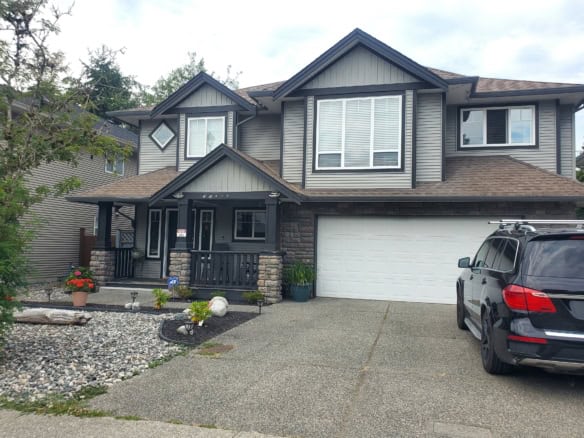 Spacious modern house with grey siding, stone accents, and a landscaped front yard in a residential neighbourhood.