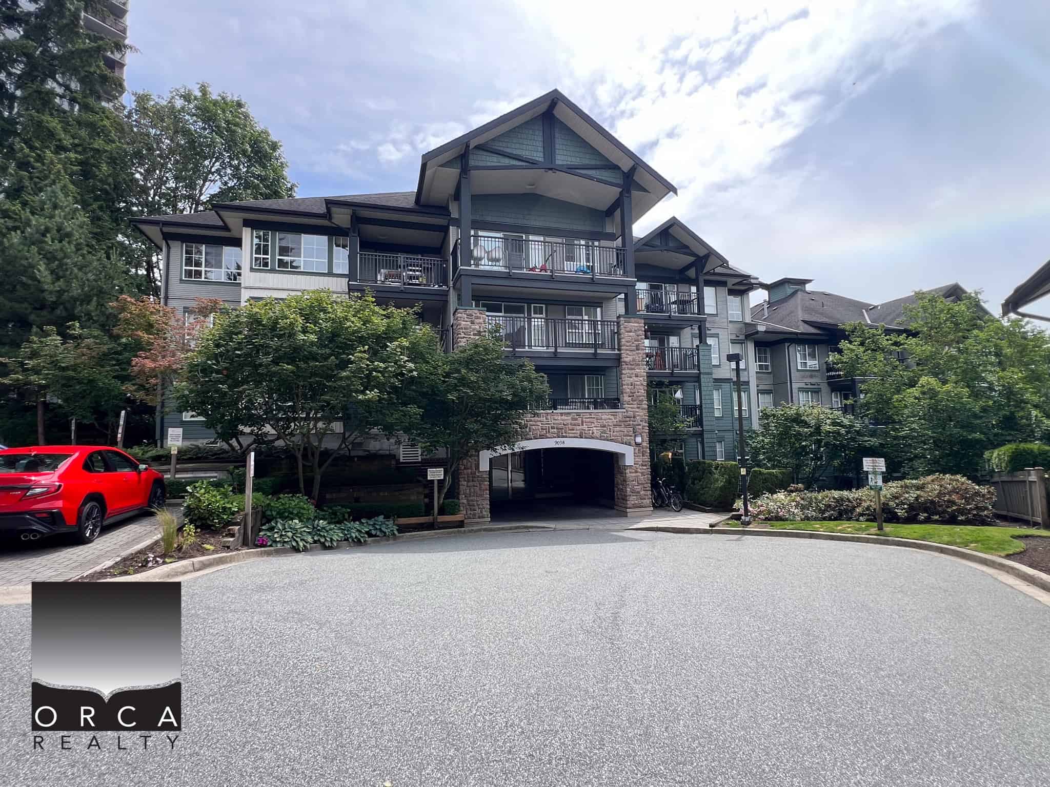 Modern multi-family residential complex with landscaped surroundings, parking lot, and multiple balconies, situated in a scenic, forested area, ideal for Vancouver housing market.