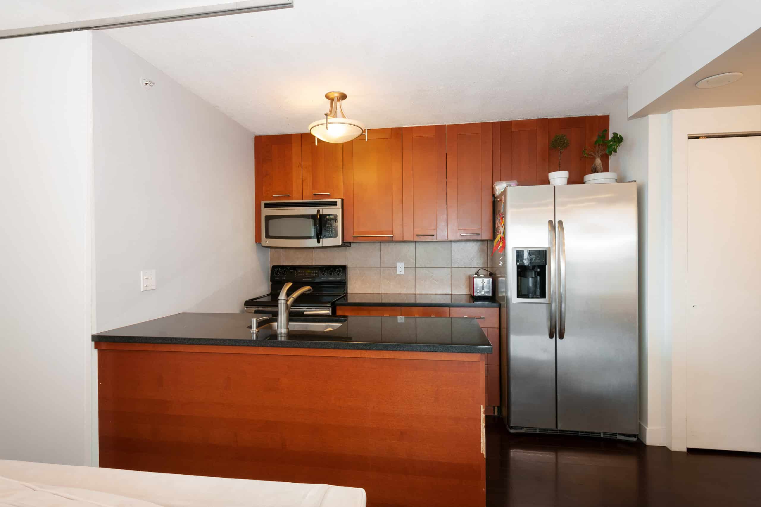 013 Modern kitchen with stainless steel refrigerator, black countertop, wooden cabinets, and stainless steel microwave, in a contemporary home offering prime real estate in Victoria, BC.