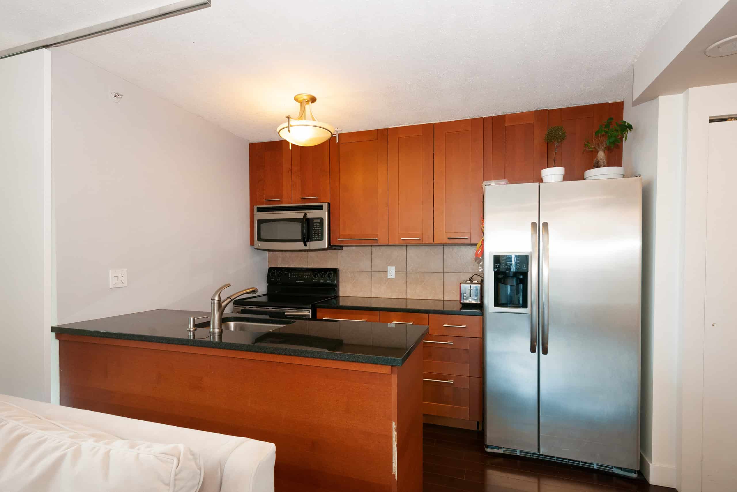 015 Modern kitchen with stainless steel refrigerator, black countertop, wooden cabinets, and energy-efficient appliances. Perfect for Vancouver real estate buyers seeking contemporary home features.