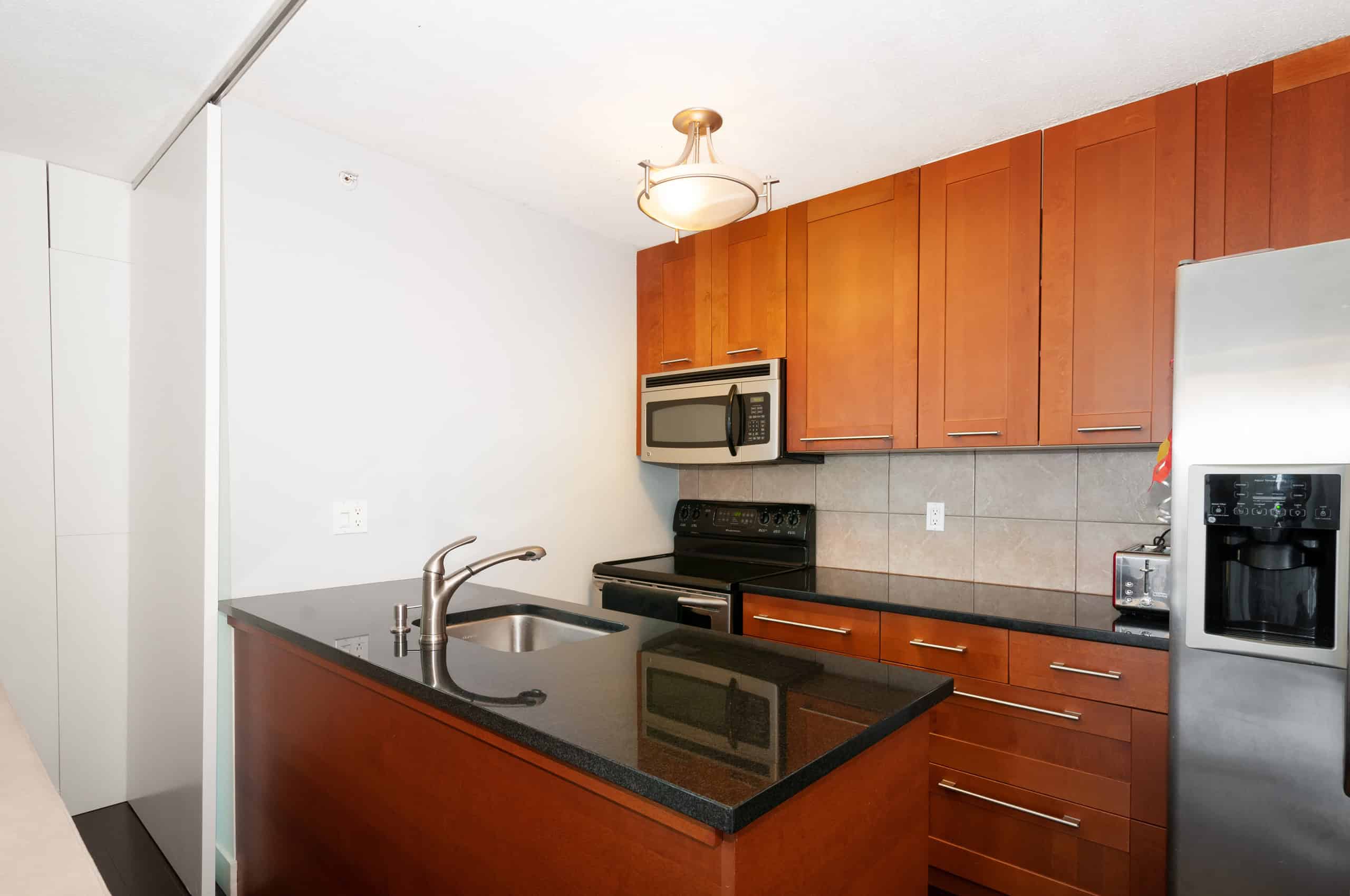 017 Modern kitchen with dark granite countertops, wooden cabinets, stainless steel appliances, including microwave, oven, and refrigerator, in a property listed by Orca Realty Inc.