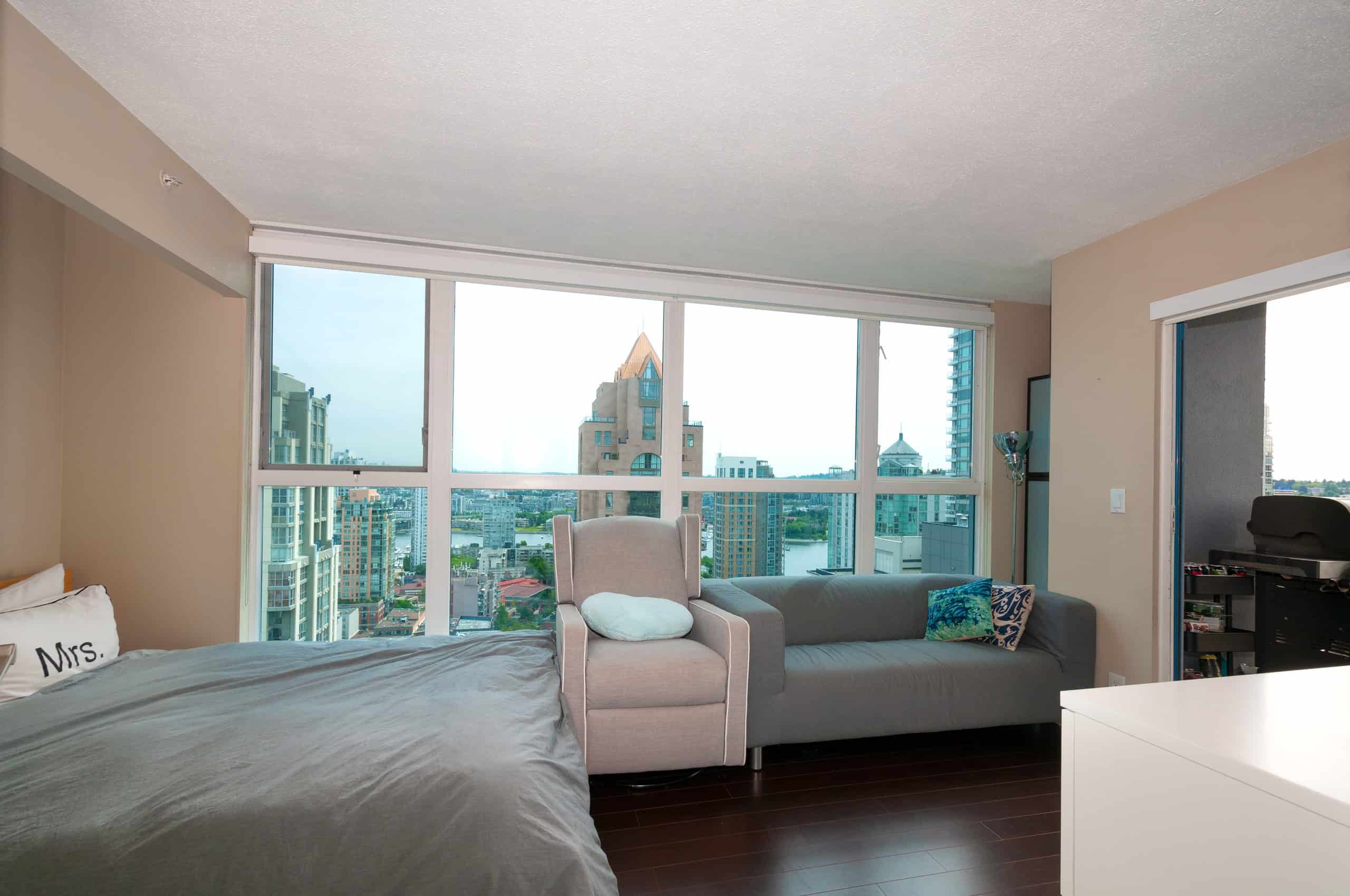 021 Modern high-rise apartment living room with city views in Vancouver, British Columbia. Bright space with large windows, comfortable furniture, and urban skyline background.