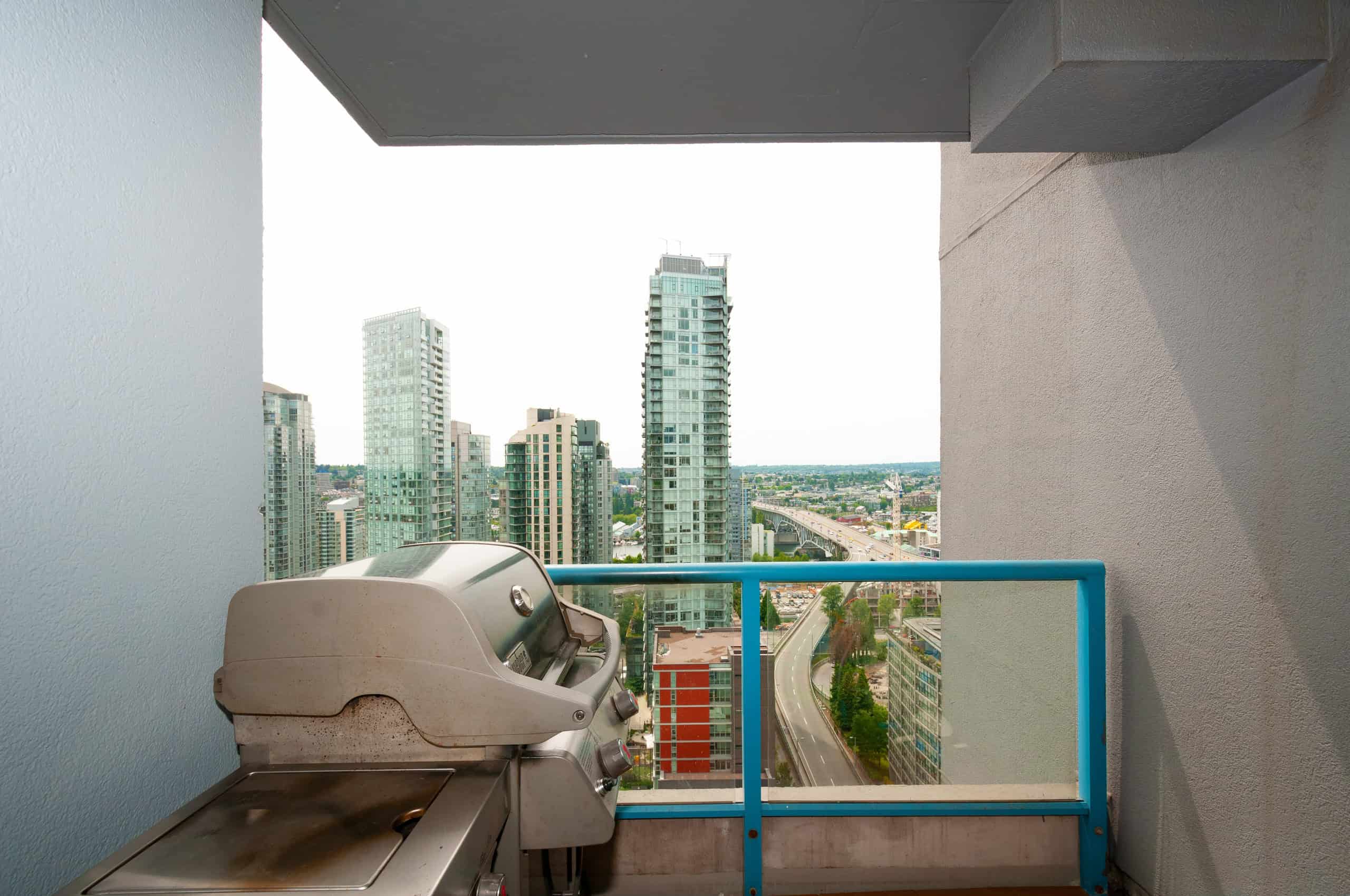 023 Stunning city skyline view from a modern condo balcony in Vancouver, British Columbia, featuring tall glass skyscrapers, urban streets, and a bright, open atmosphere.