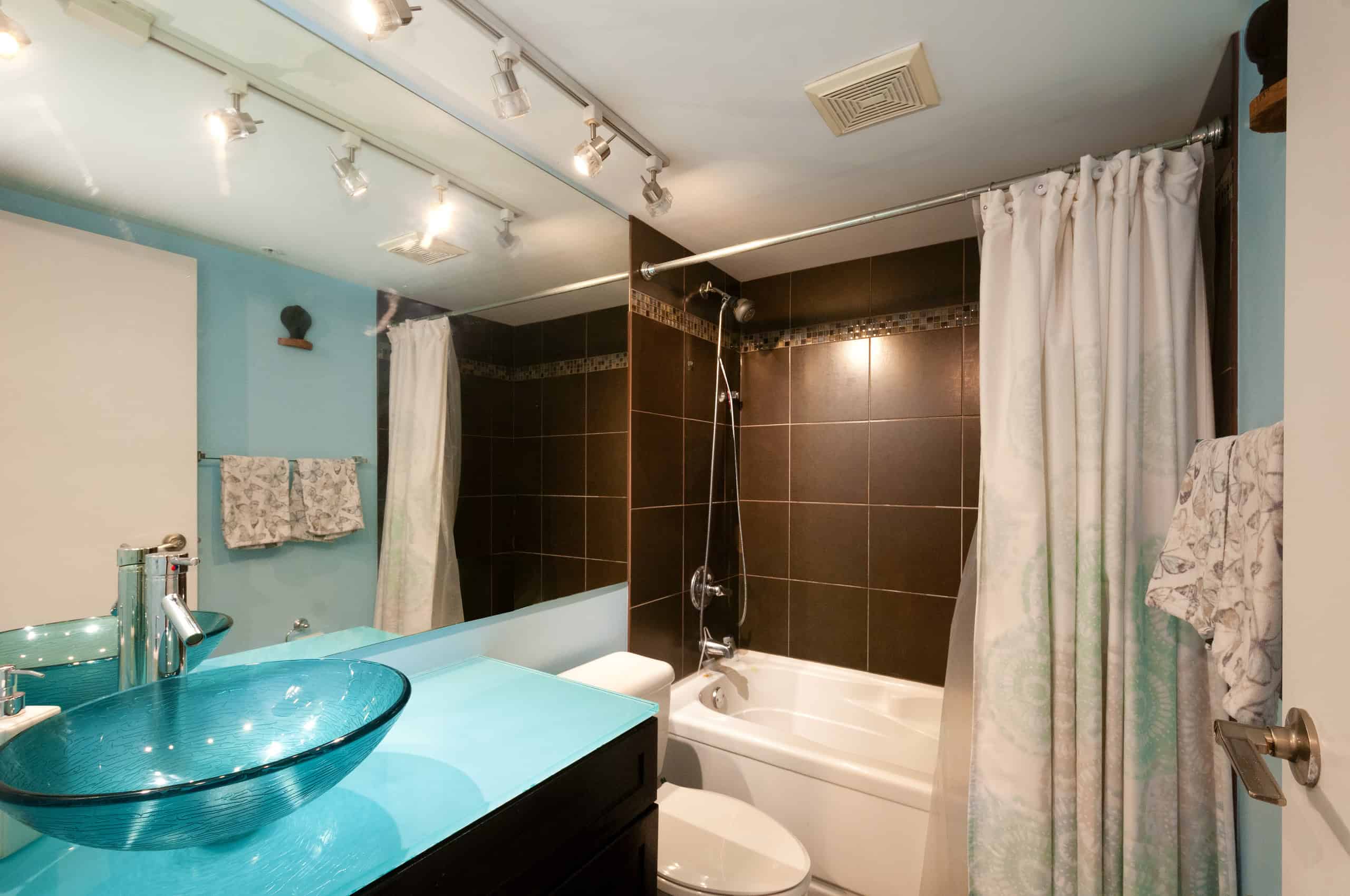 041 Modern bathroom with a turquoise vessel sink, dark tiled shower/bathtub combination, and bright lighting, showcasing contemporary bathroom fixtures and decor.