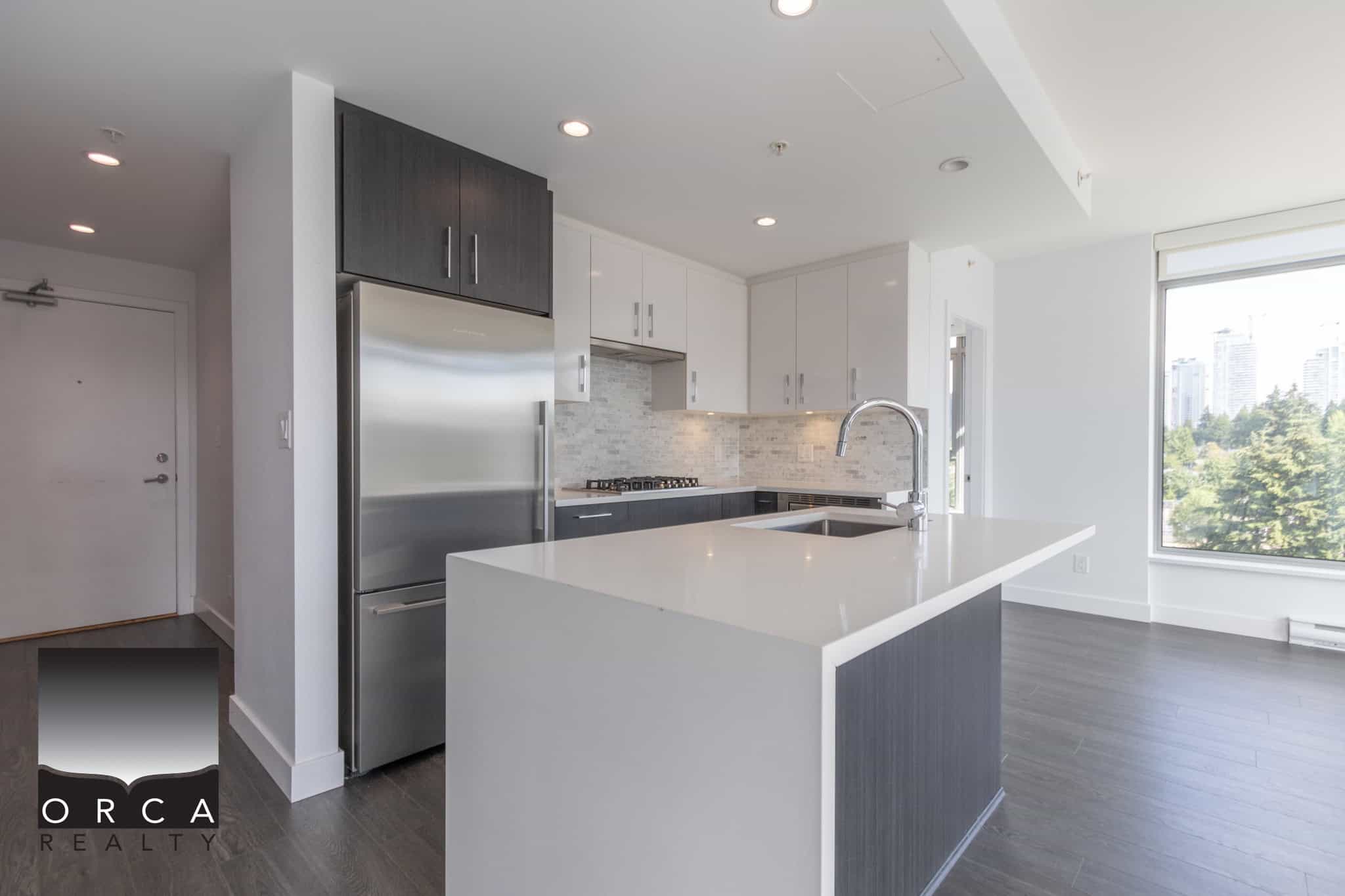 Spacious modern kitchen with white cabinetry, stainless steel appliances, and a large island, showcasing contemporary urban living in Vancouver, BC, ideal for real estate buyers and investors.