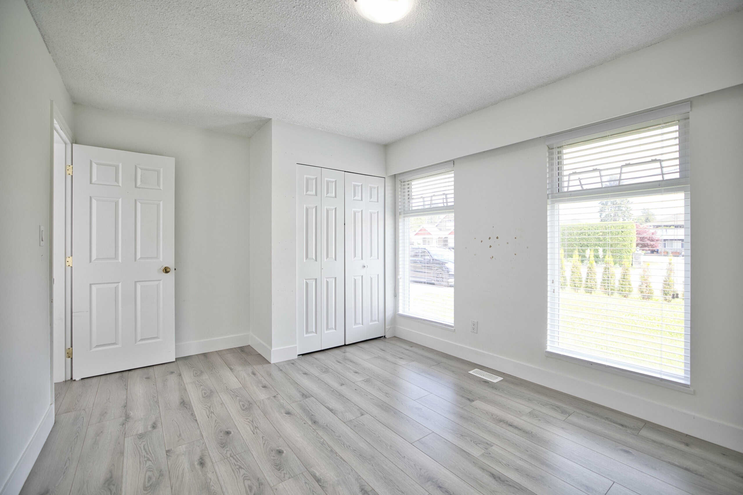 Bright, empty bedroom in a modern Vancouver home with large windows, white walls, and light wood flooring—ideal for a peaceful and stylish living space in Vancouver.