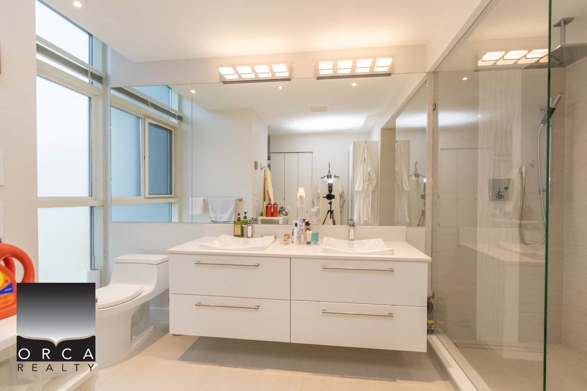 Bright modern bathroom with double vanity, walk-in shower, and large mirror, showcasing contemporary design and high-end fixtures at Orca Realty Inc. Vancouver real estate.