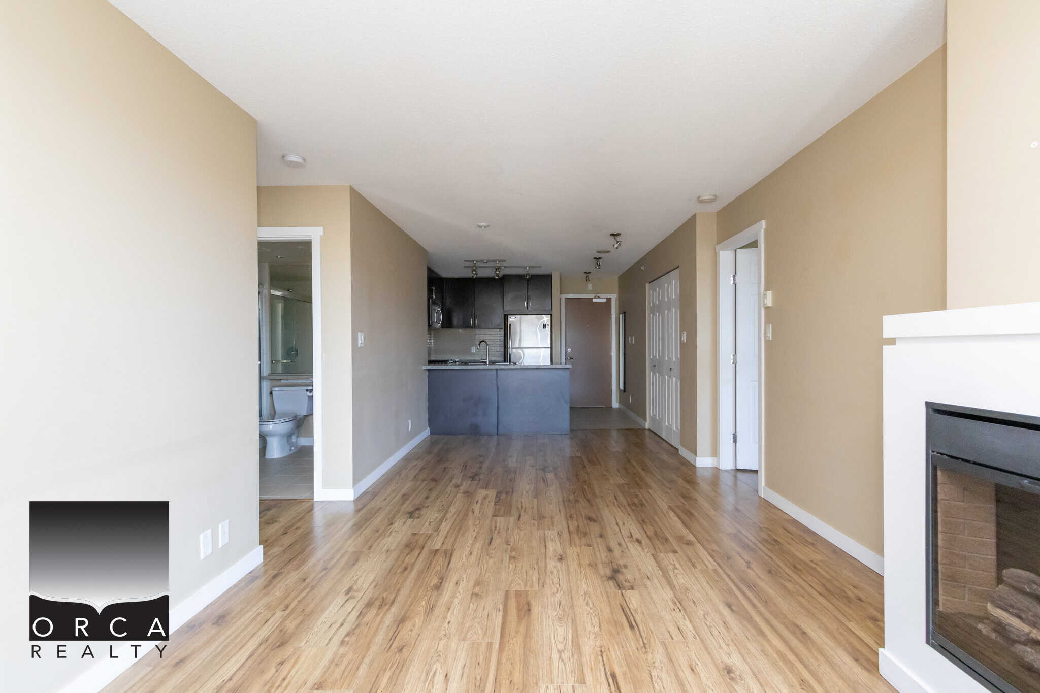 Spacious apartment living room with hardwood flooring, modern kitchen, and cozy fireplace, ideal for Vancouver real estate buyers seeking contemporary condo comfort.