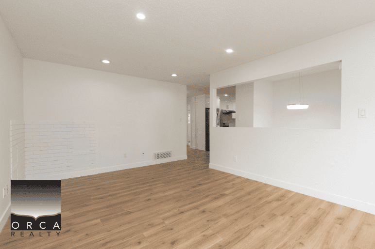 White interior living room with hardwood flooring, modern lighting, and open space, perfect for real estate listings or home staging by Orca Realty Inc.