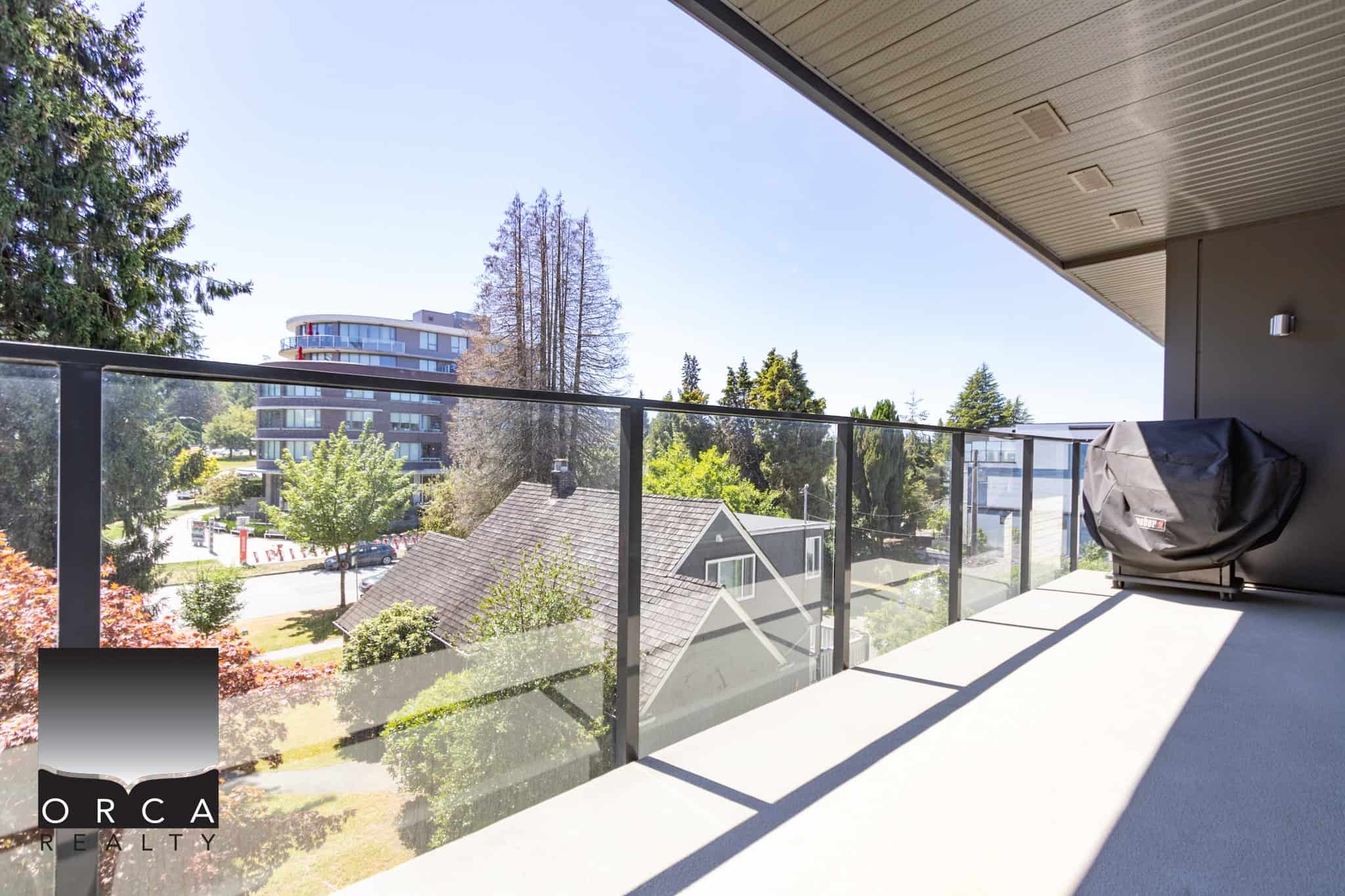 Modern balcony with glass railing and scenic views of a residential neighborhood and lush trees in Vancouver, British Columbia, showcased by Orca Realty Inc.