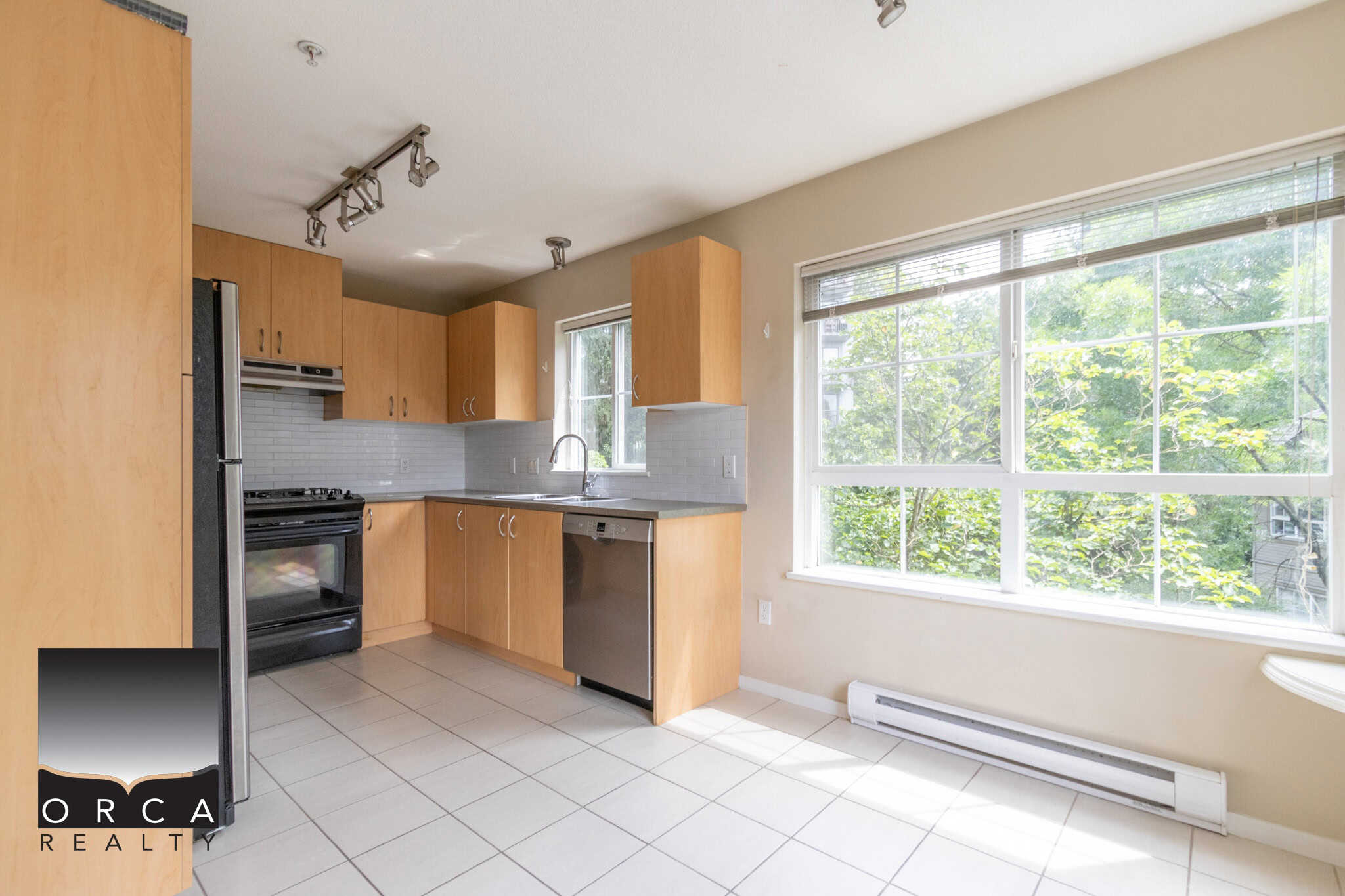 Bright modern kitchen with wooden cabinets, stainless steel appliances, large windows with lush green view, ideal for Vancouver or Victoria real estate listings.