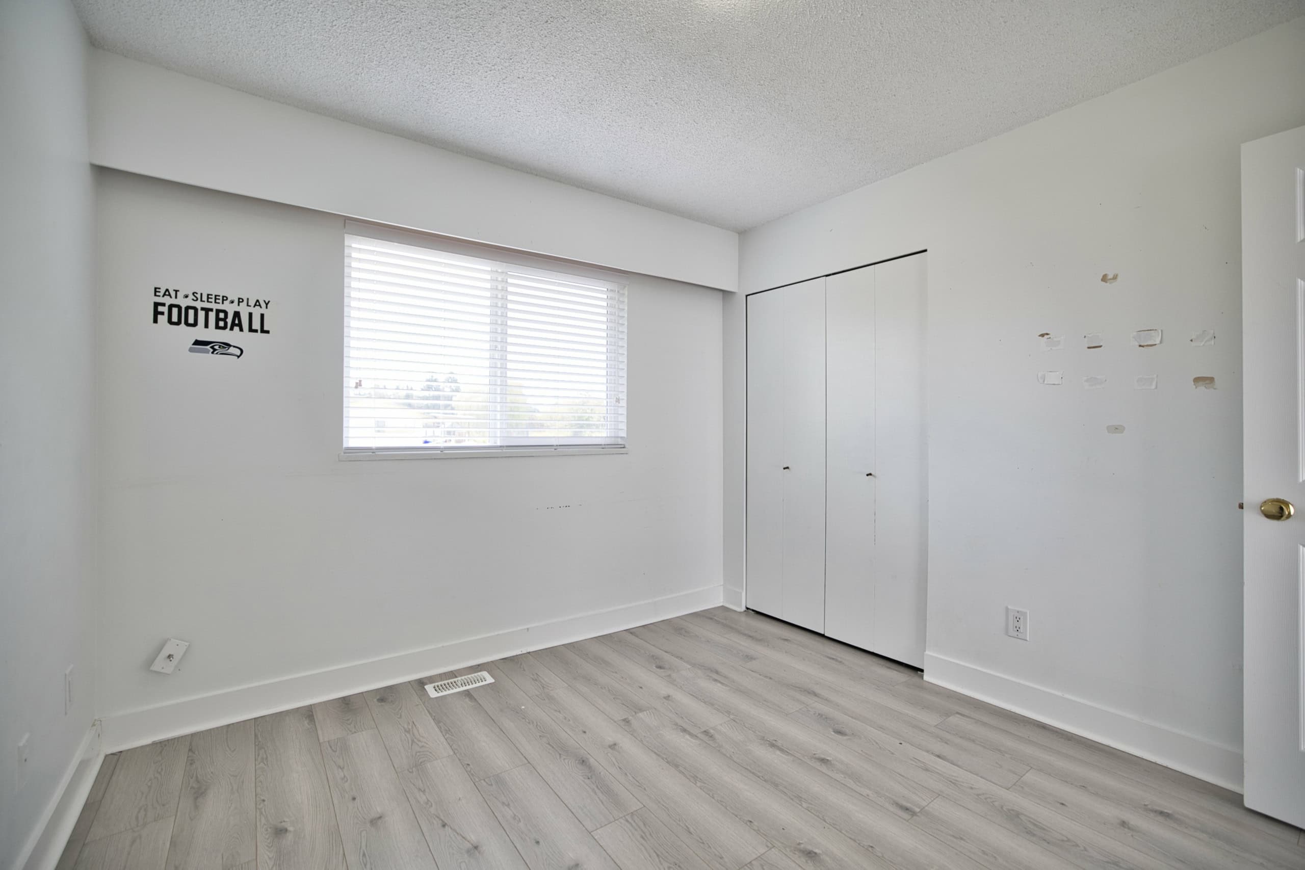 Bright empty bedroom with white walls, large window with blinds, closet space, and light wood flooring, showcasing a clean and modern interior ideal for Vancouver-area homes.