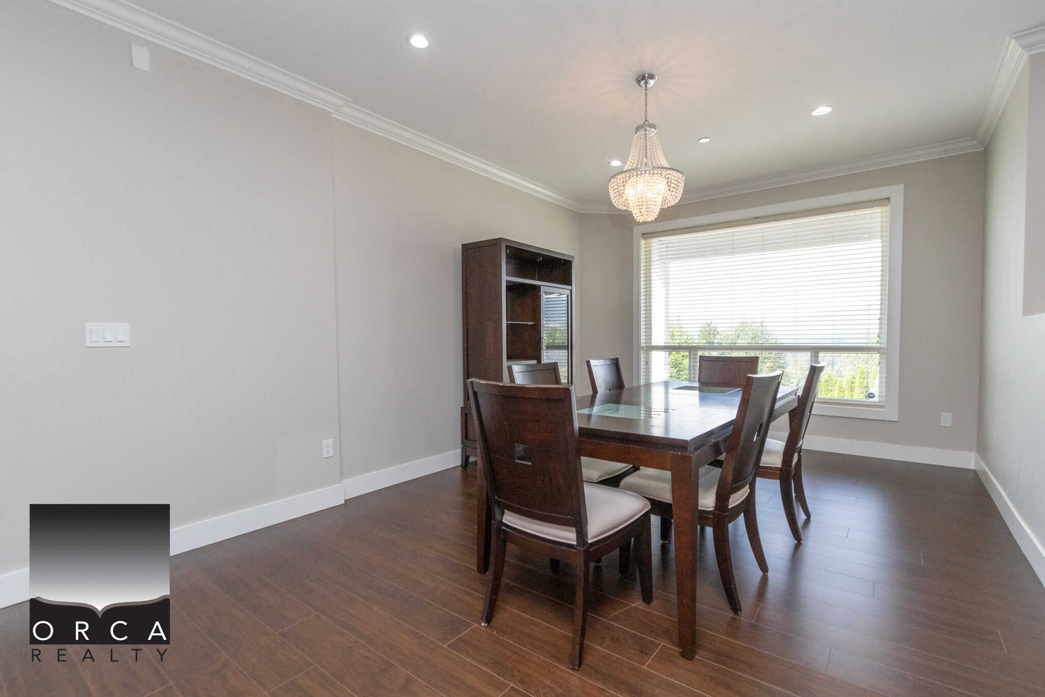 Bright dining room with large window, modern chandelier, hardwood flooring, and neutral wall colors, ideal for family gatherings and entertaining in Vancouver real estate.