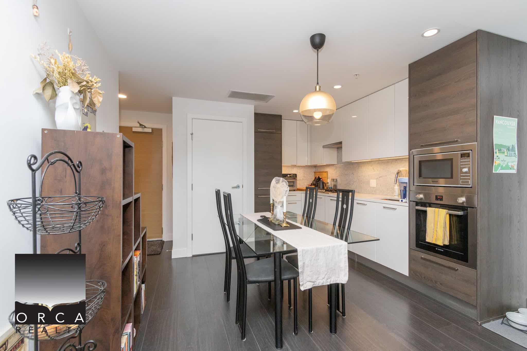 Modern kitchen and dining area in Vancouver condo with sleek white cabinets, stainless steel appliances, and dark hardwood flooring, perfect for contemporary urban living.
