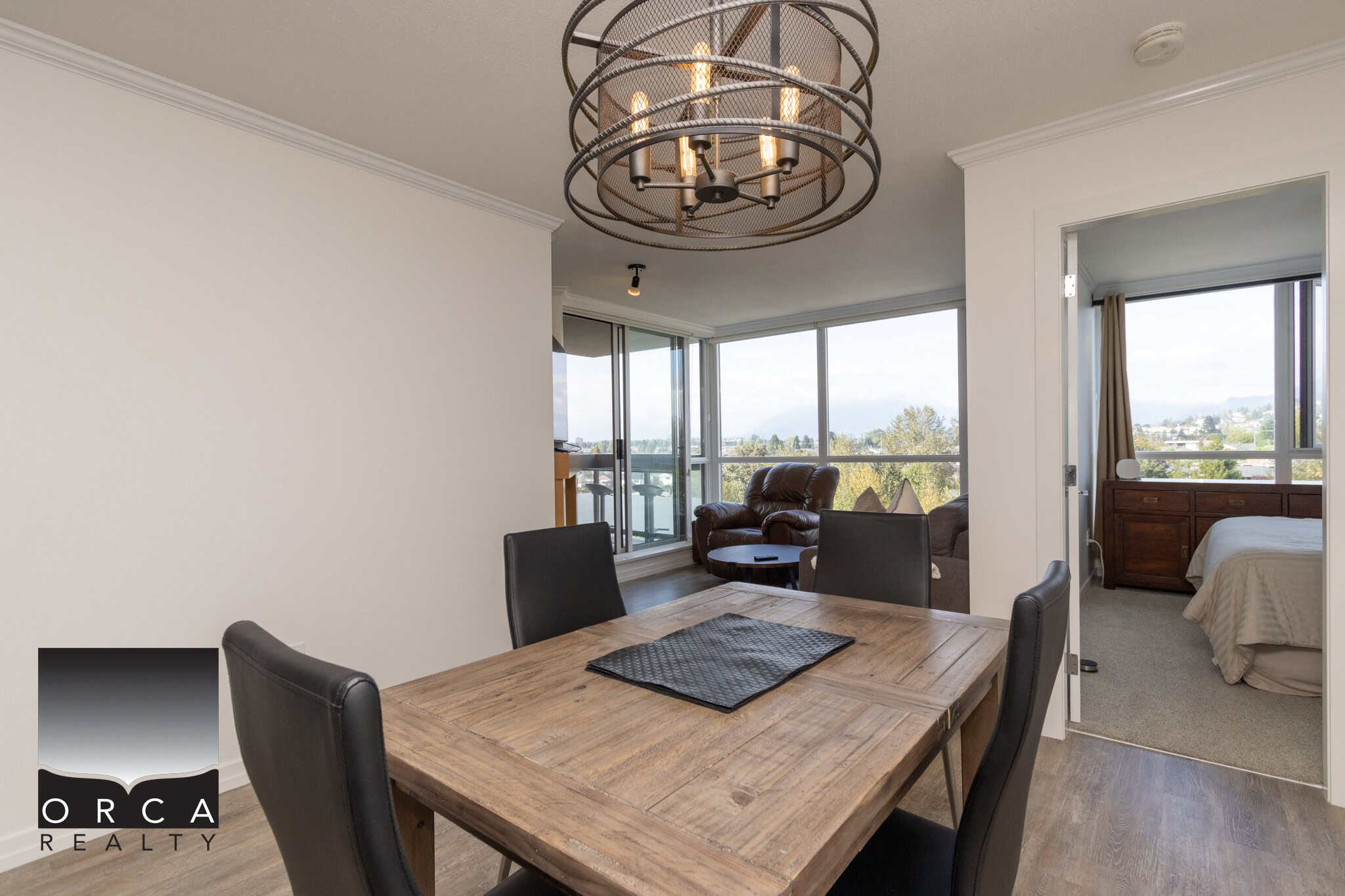 Modern dining area with wooden table, black chairs, and a stylish chandelier in a contemporary condo with large windows and panoramic city views in Vancouver.