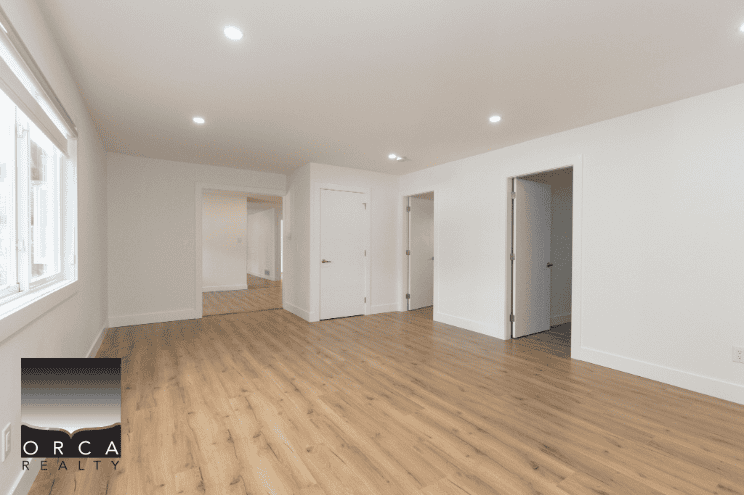 Bright modern empty living room with hardwood floors, white walls, and large windows, showcasing a clean and spacious interior ideal for buyers looking for contemporary real estate options in BC.