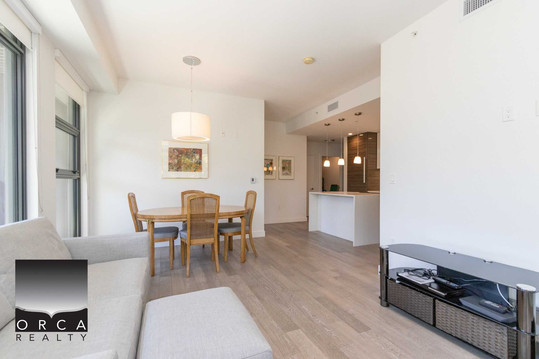 Bright open-concept living and dining area in a modern condo, featuring hardwood floors, large windows, and stylish furnishings, ideal for comfortable Vancouver Island living.