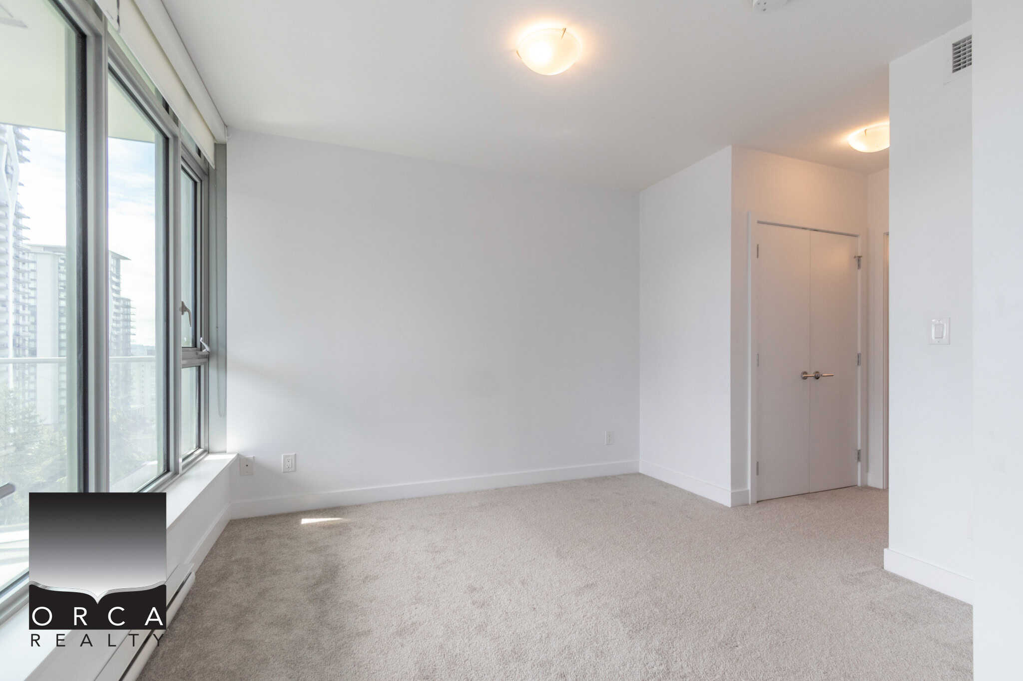 Bright modern living room in a Vancouver condominium with large windows and natural light, ideal for urban living, featuring neutral carpet flooring and fresh white walls, perfect for real estate listings.