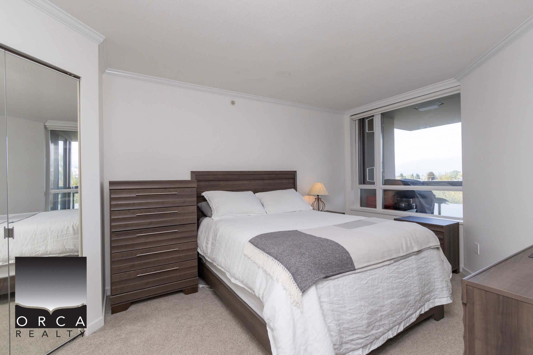 Cozy modern bedroom with large window, stylish wooden furniture, and neutral decor, ideal for Vancouver condo living, available through Orca Realty Inc. in BC.