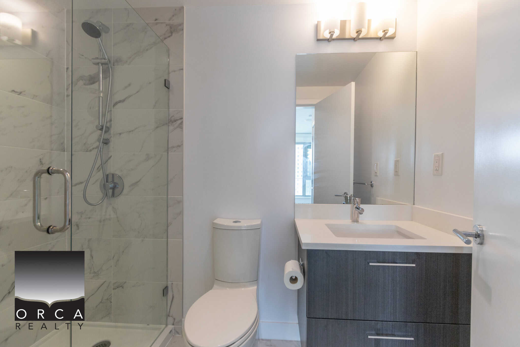 Modern bathroom in a contemporary condo featuring a glass-enclosed shower, sleek vanity with a large mirror, and neutral colour palette, ideal for downtown Vancouver living.
