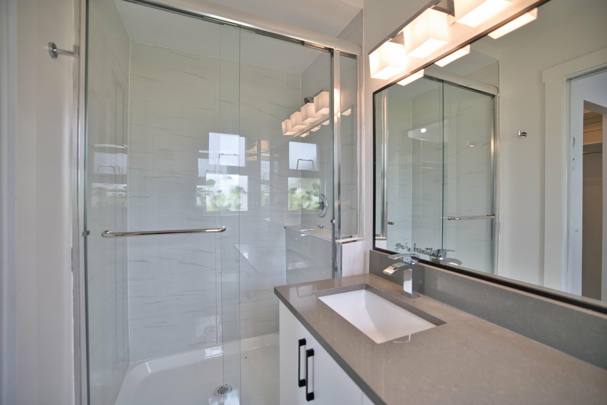Bright modern bathroom with glass shower enclosure, white tiled walls, and a sleek vanity with a large mirror, ideal for showcasing contemporary Vancouver real estate.