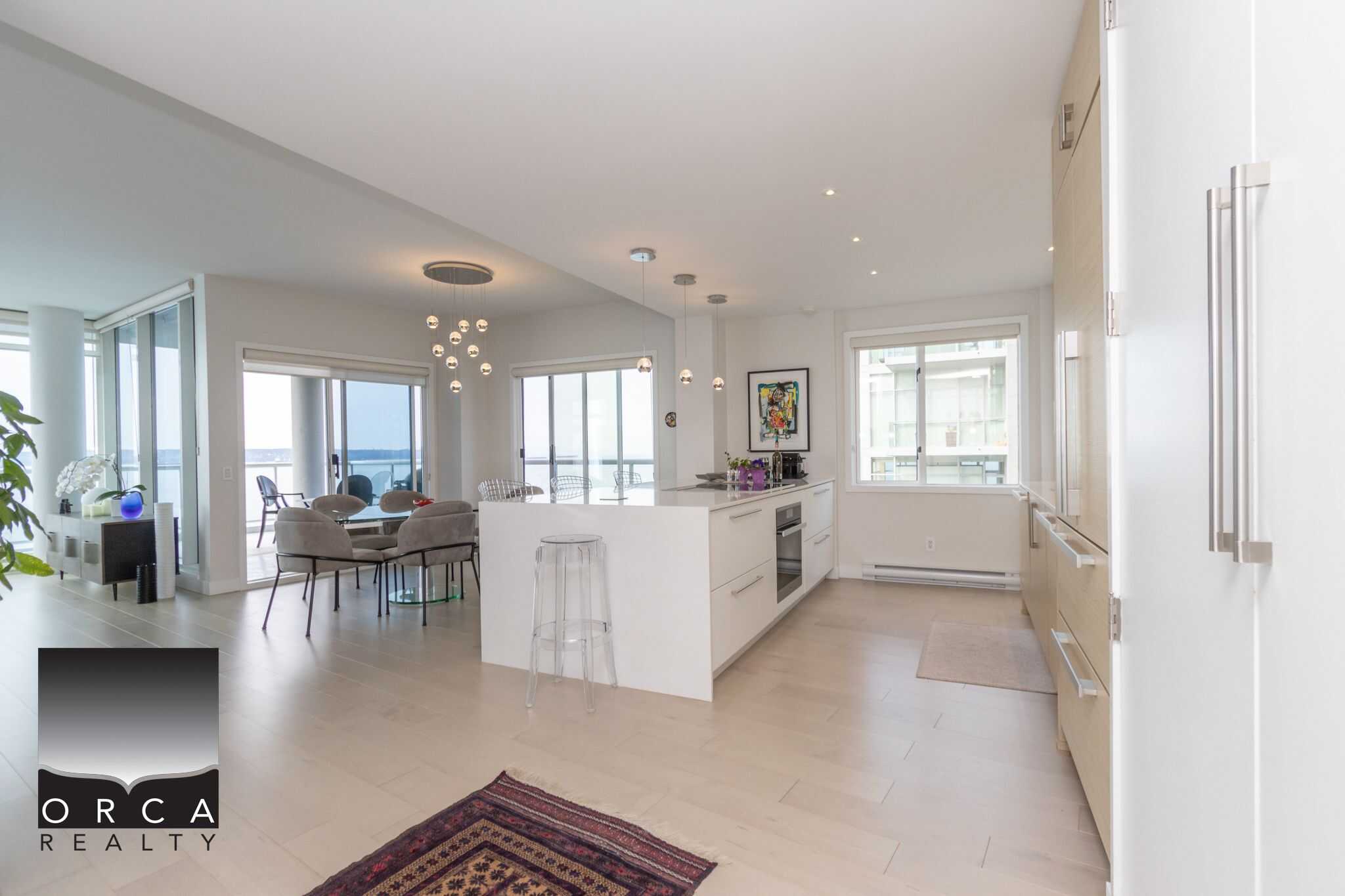 Spacious modern open-plan condo kitchen and living area with large windows, contemporary furnishings, and ocean views, featuring sleek cabinetry, minimalist decor, and lots of natural light.