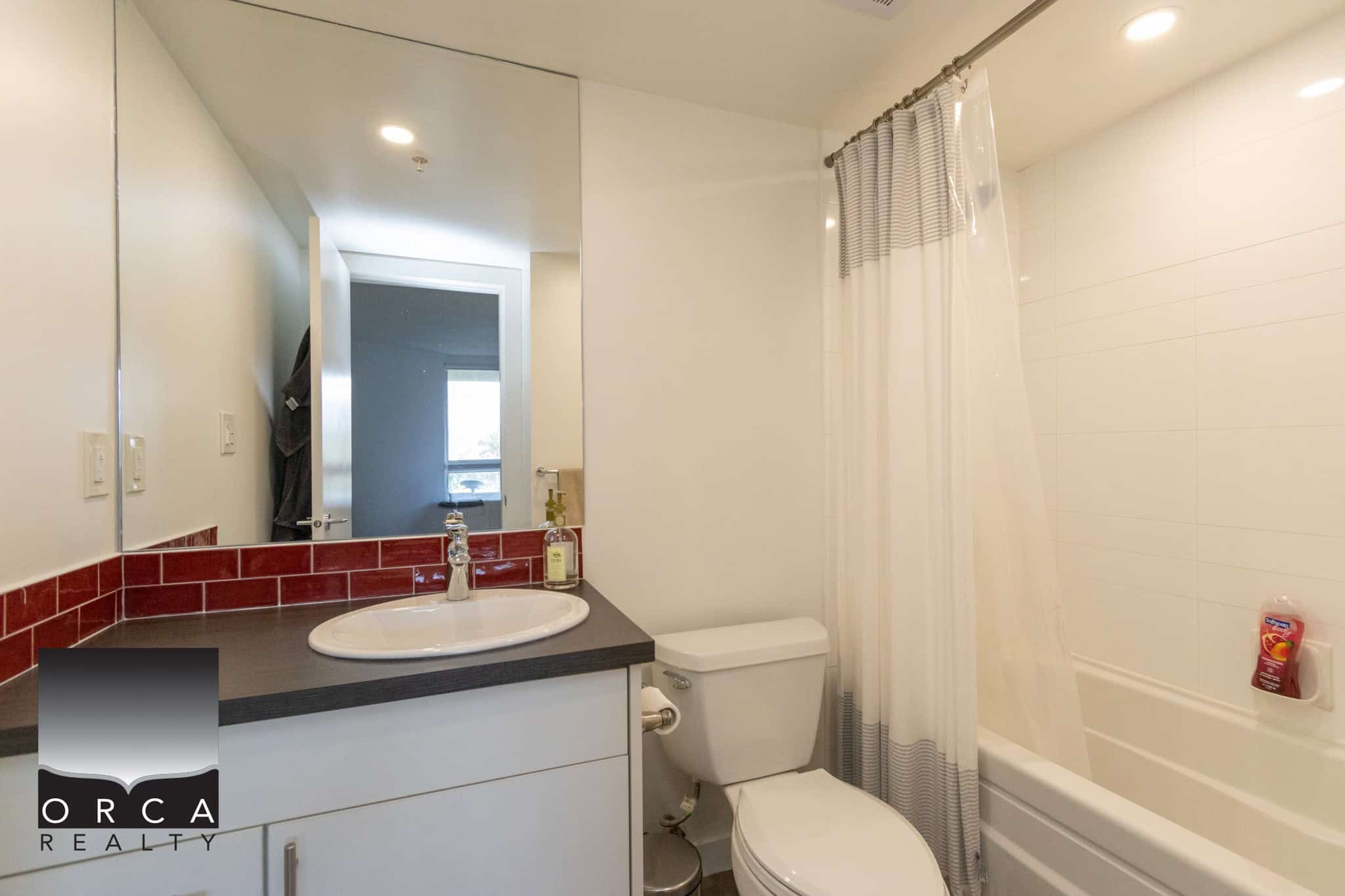 Modern bathroom with white fixtures, shower and bathtub, sleek vanity with red backsplash tiles, Ideal for Vancouver condos or apartments near Orca Realty Inc.