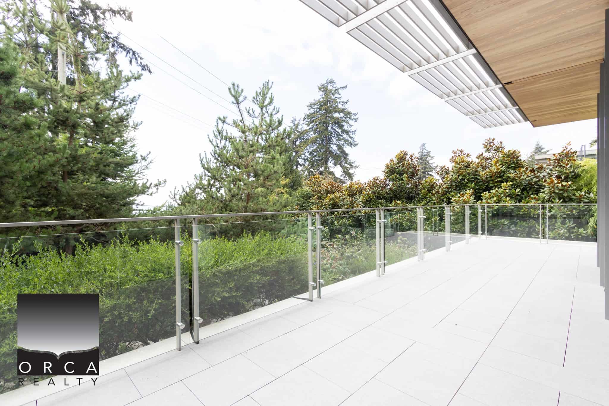 Spacious modern balcony with glass railing overlooking lush greenery and trees, ideal for outdoor living and relaxation; part of premium Orca Realty Inc. property listings.