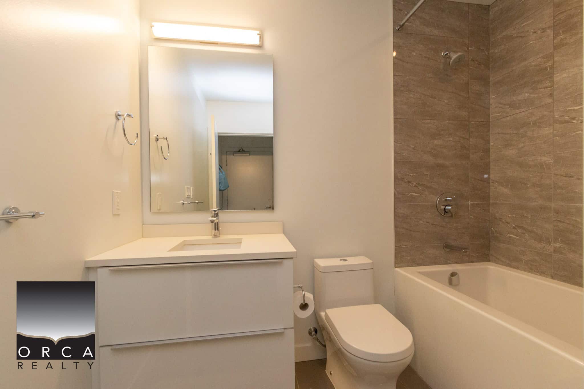 Modern bathroom with white vanity, large mirror, bathtub with beige tile surround, and updated fixtures, ideal for Vancouver Island real estate buyers seeking stylish homes.