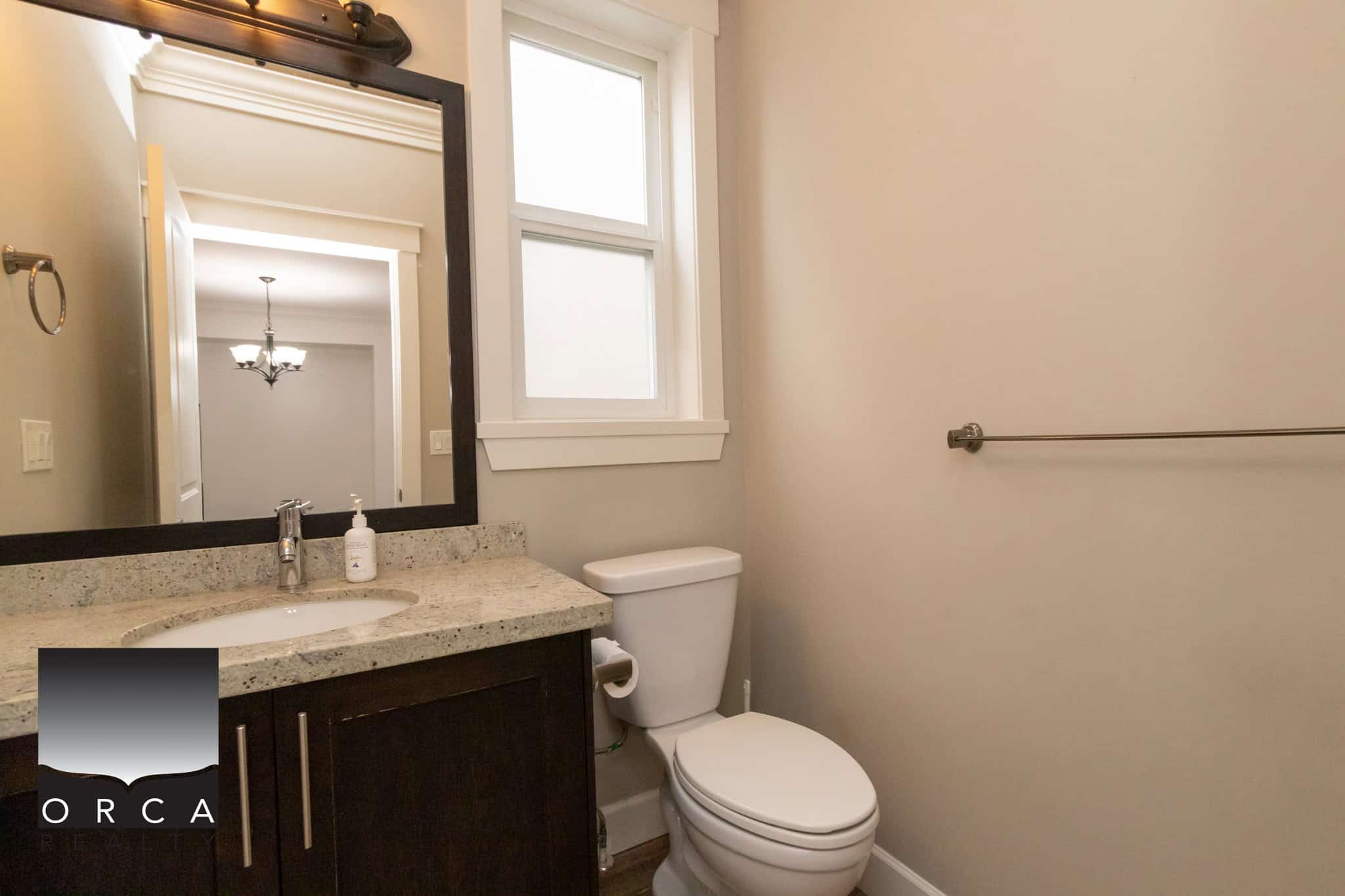 Modern bathroom with granite countertop vanity and white toilet, featuring a large mirror, natural light from double-hung window, and neutral wall tones, ideal for Vancouver real estate listings.