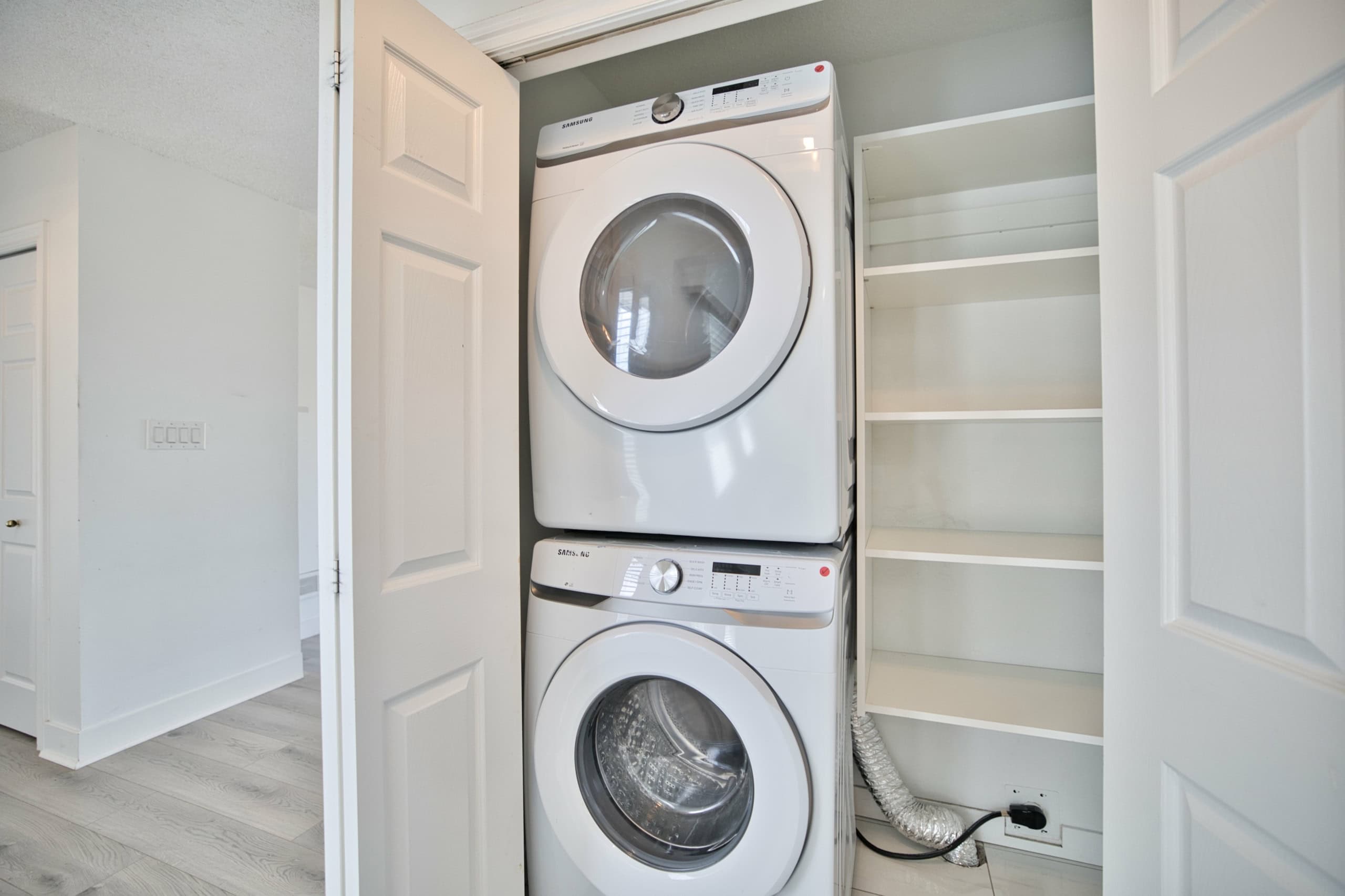 Clean stacked washer and dryer in a bright laundry room with white shelving, showcasing modern appliances and ample storage space at Orca Realty Inc.