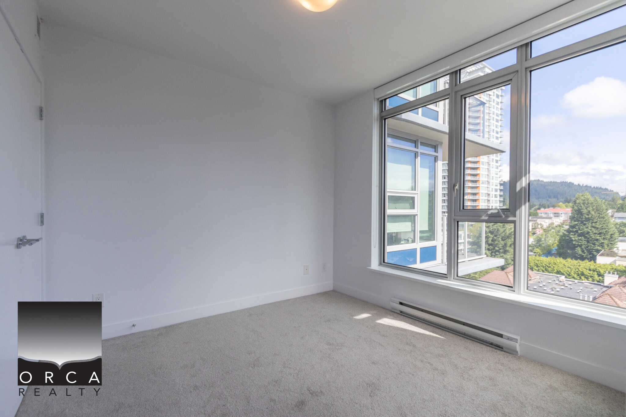 Bright modern apartment room with large windows showcasing city and mountain views, featuring neutral carpet, open space, ideal for Vancouver real estate buyers.