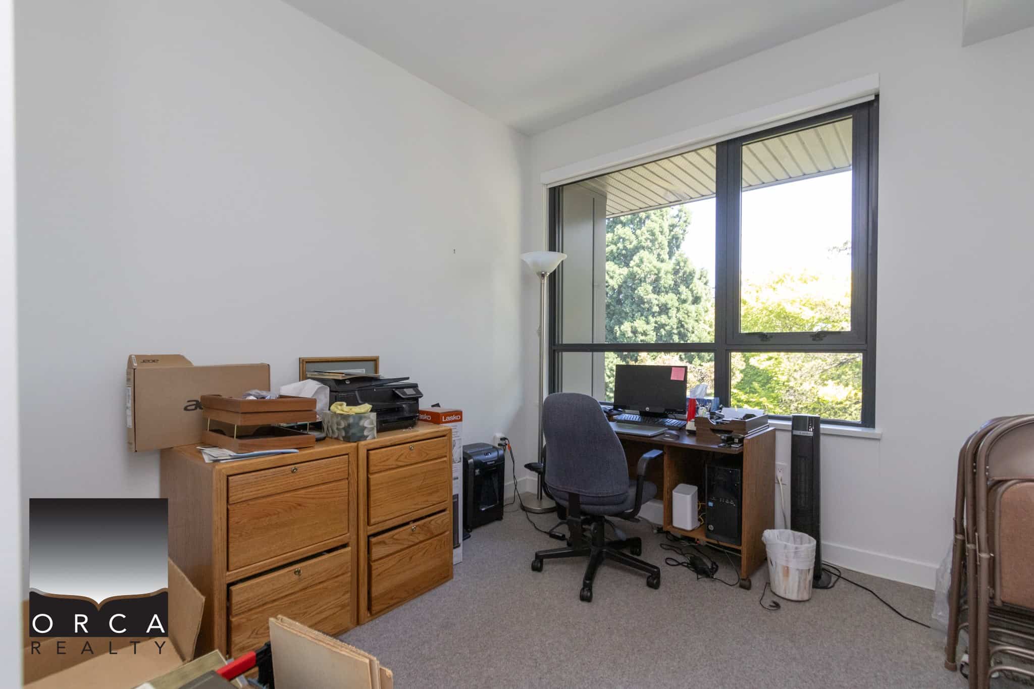 Unhome office space with desk, computer, window view of green trees, and office supplies, showcasing a functional workspace for real estate professionals in Vancouver.
