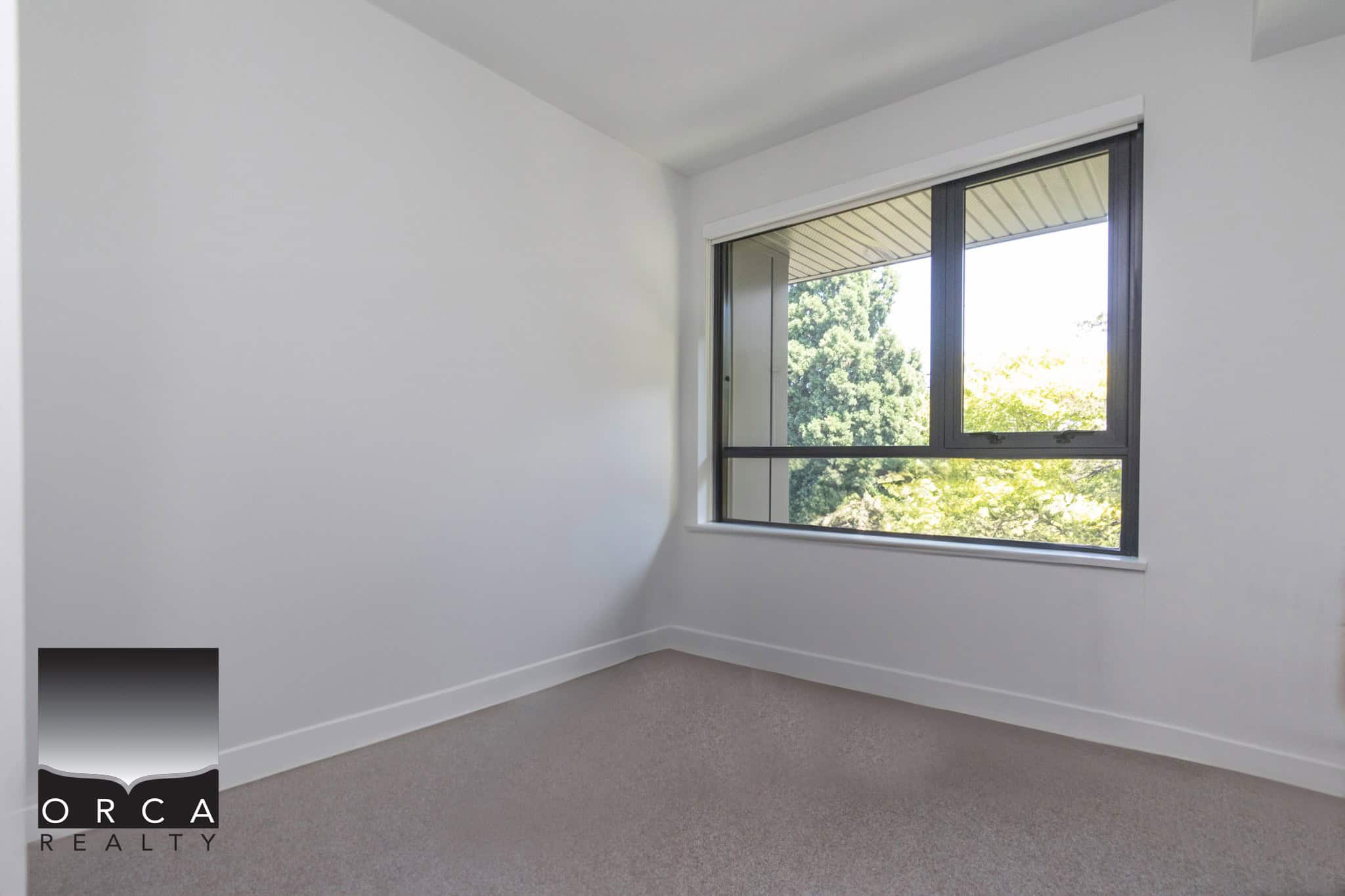 Bright modern bedroom with large window, neutral wall colour, and clean carpet flooring in a residential property listed by Orca Realty Inc. for prospective homebuyers.
