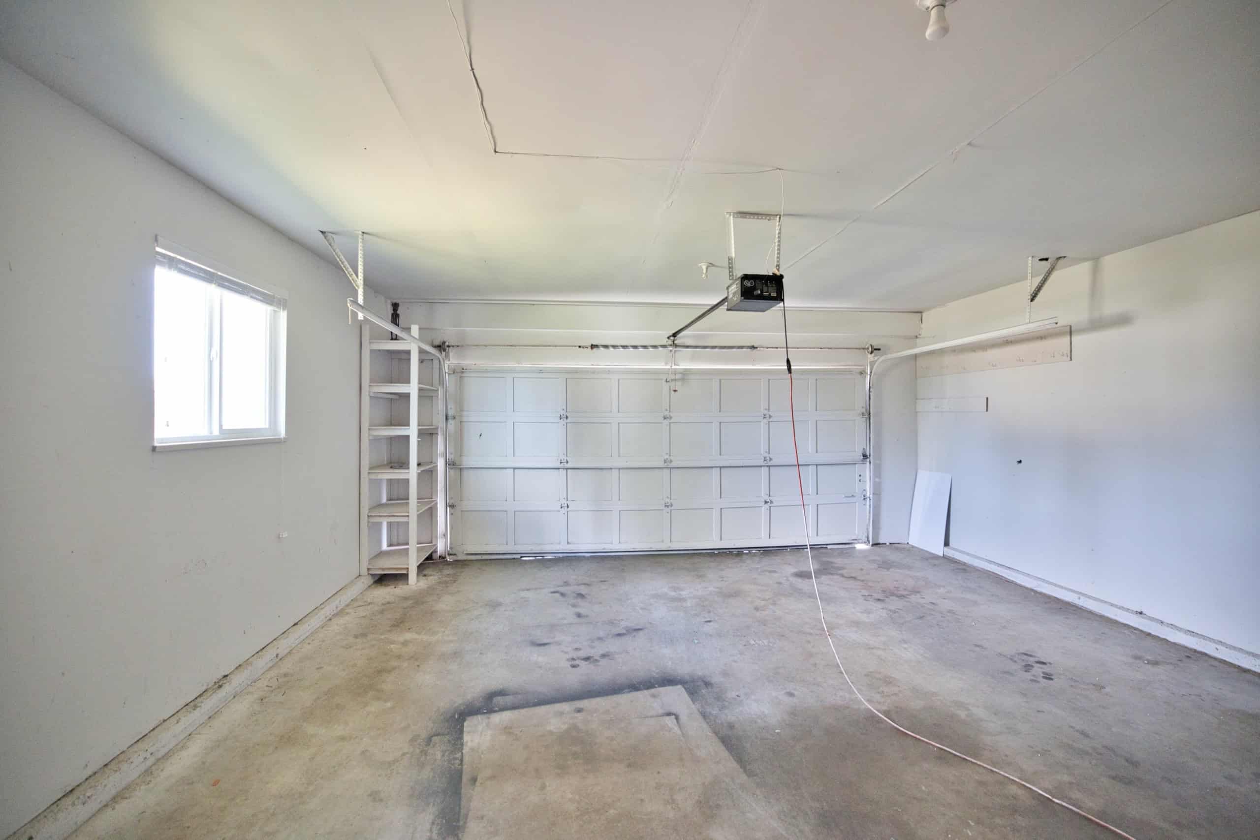 Spacious garage with a white sectional door, natural light from windows, and open floor space, perfect for vehicle storage or workshop use.