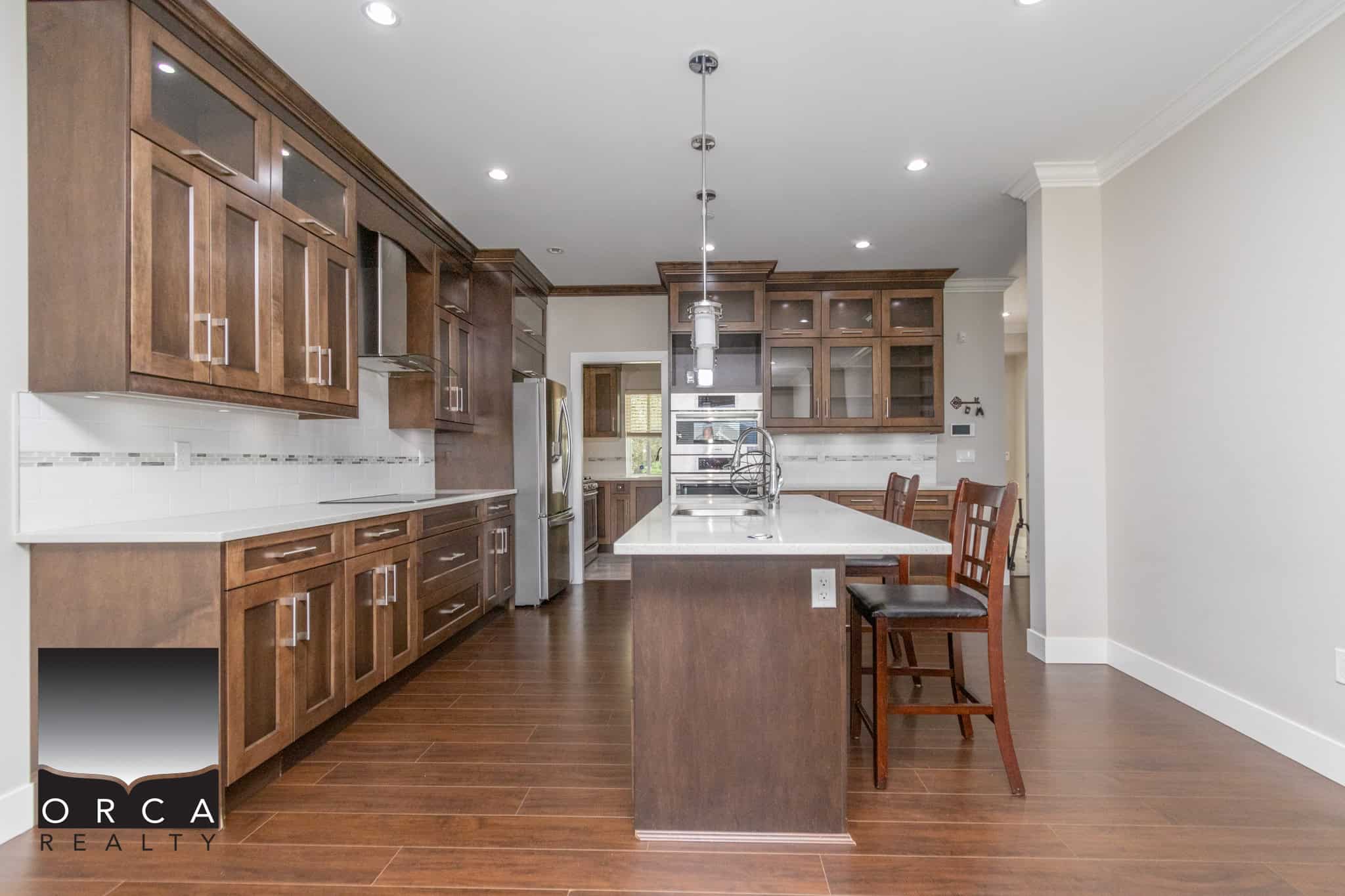 Spacious modern kitchen with dark wooden cabinetry, white countertops, stainless steel appliances, and a large kitchen island, ideal for family living and entertaining.